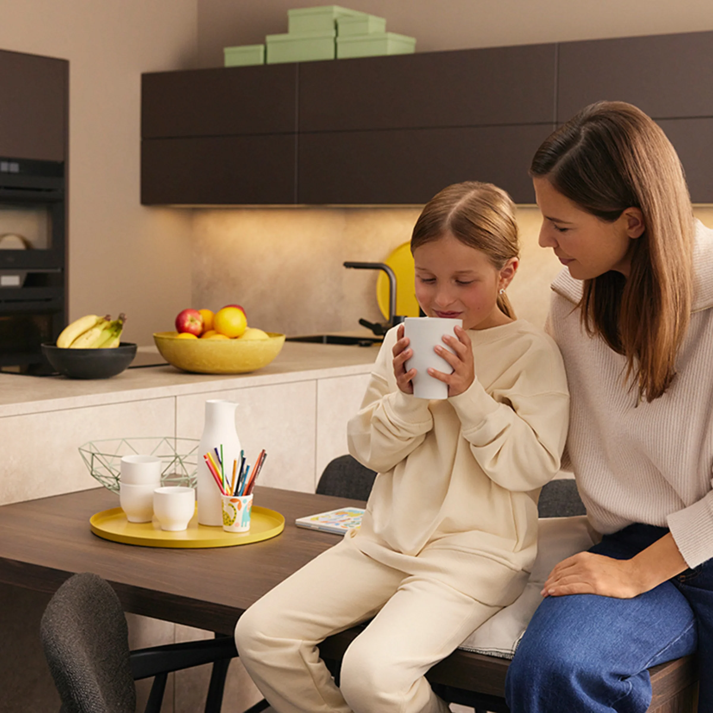 Una donna e un bambino seduti in una cucina moderna di Nolte Kitchen, il bambino tiene una tazza.