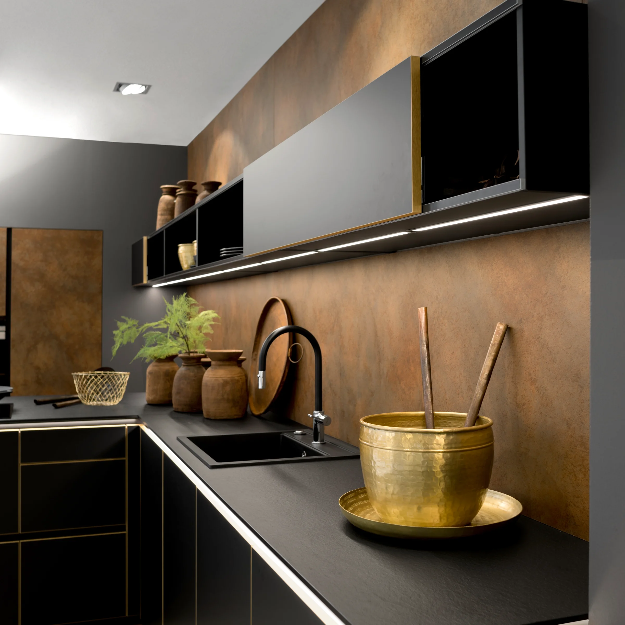 Modern kitchen with black cabinets, gold accents, and plants. Nolte Kitchen.