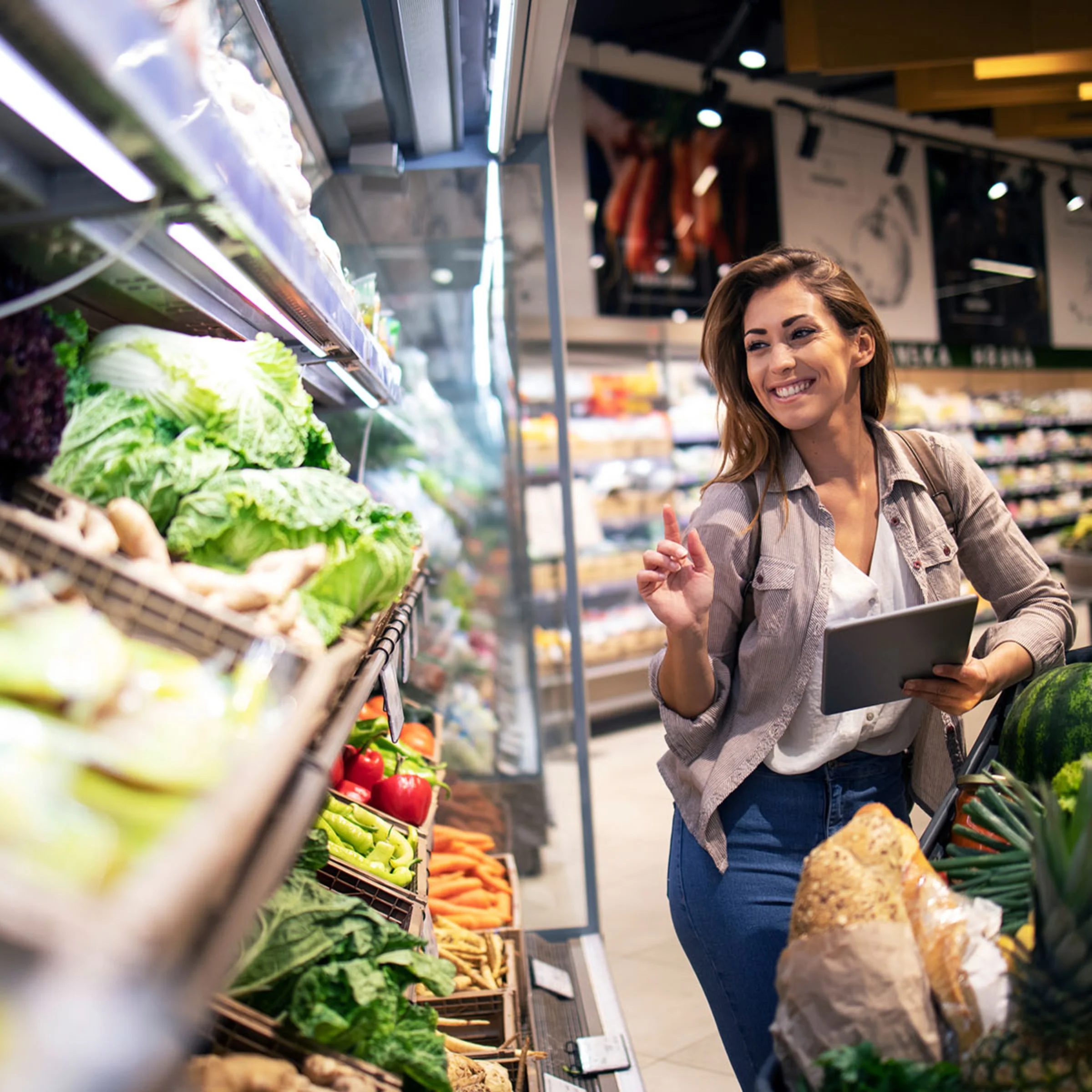 Una donna sceglie verdure fresche in un supermercato mentre tiene un tablet.