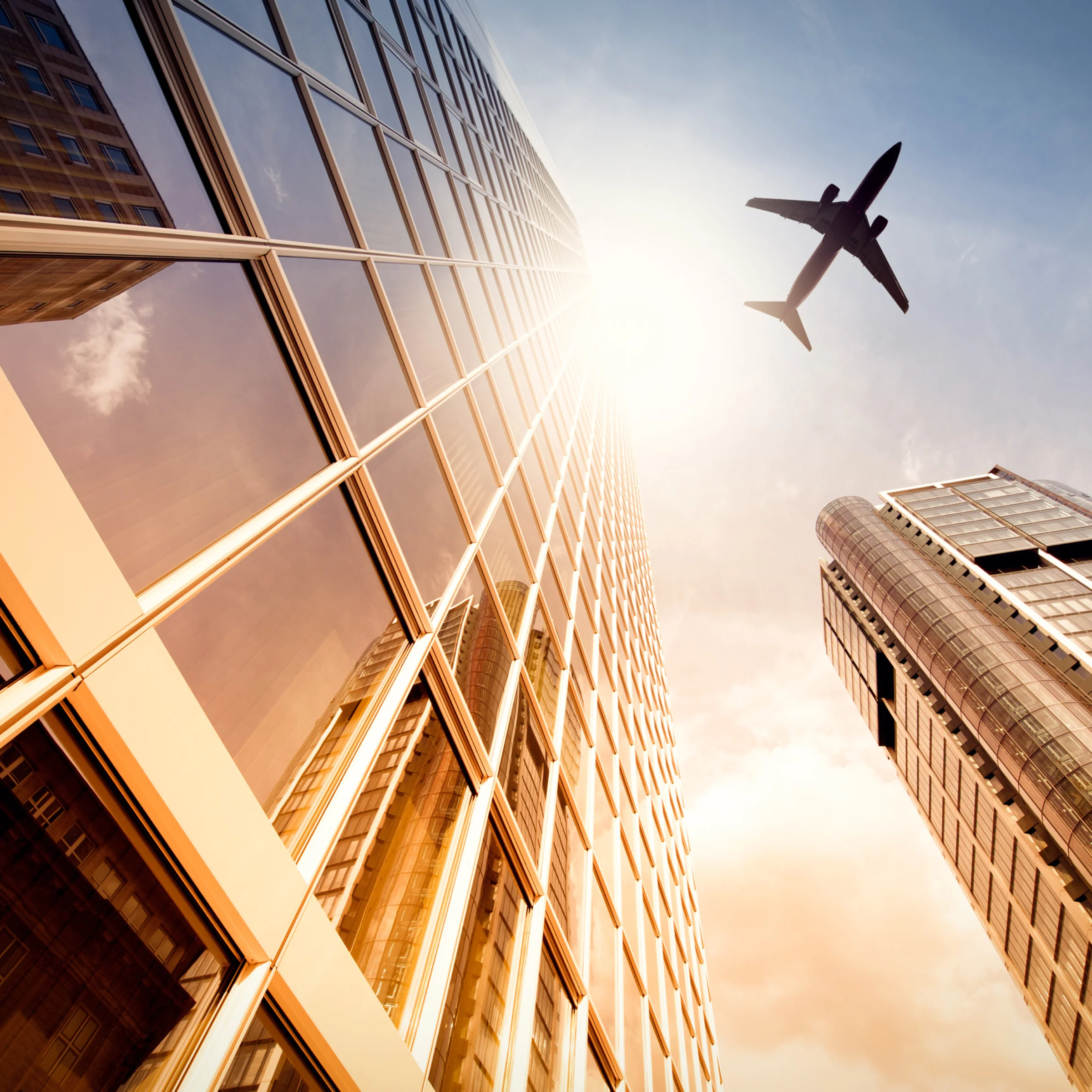 Un aereo vola sopra grattacieli moderni in una città al tramonto.