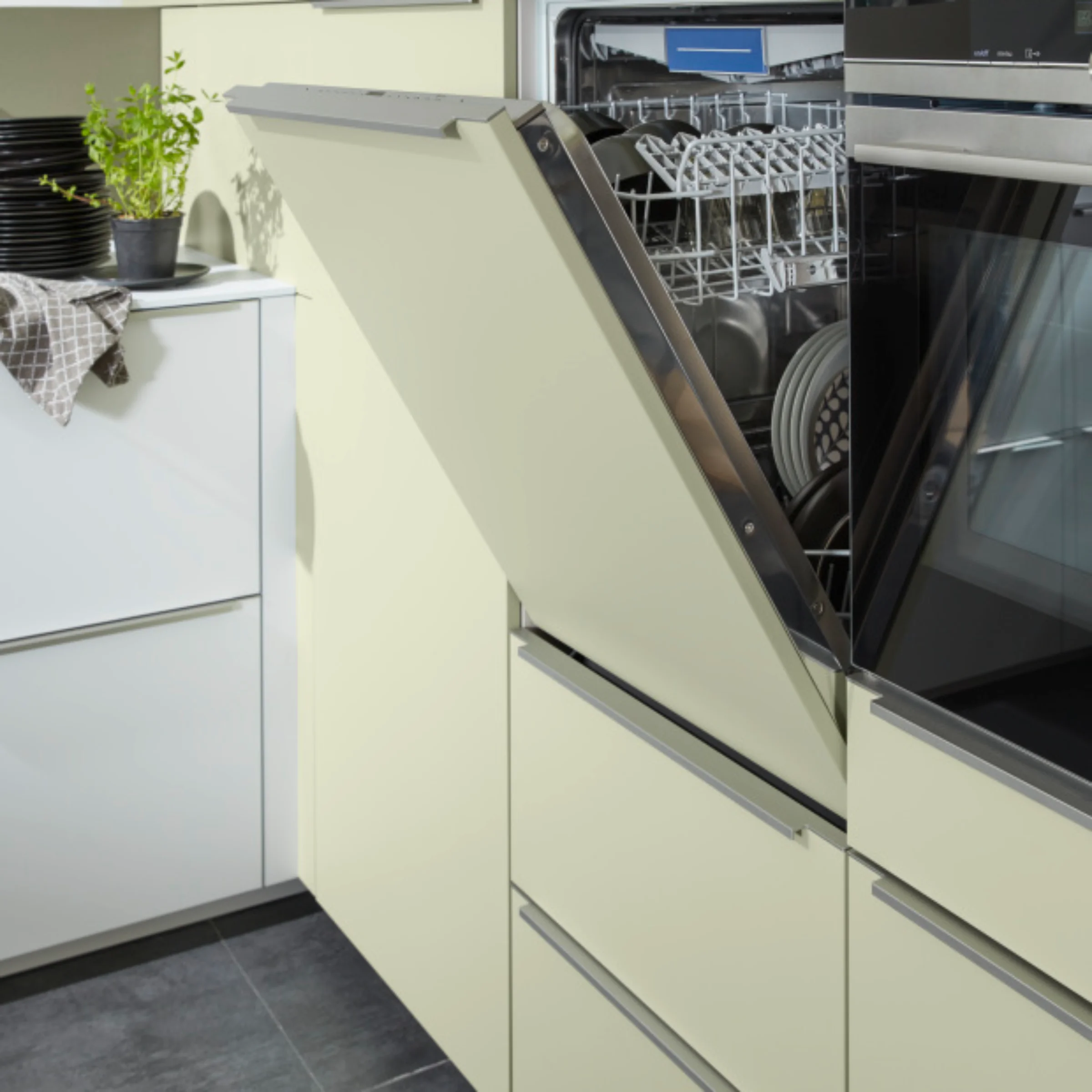Lavastoviglie aperta in una cucina moderna con armadi chiari, piante e stoviglie. Nolte Kitchen.