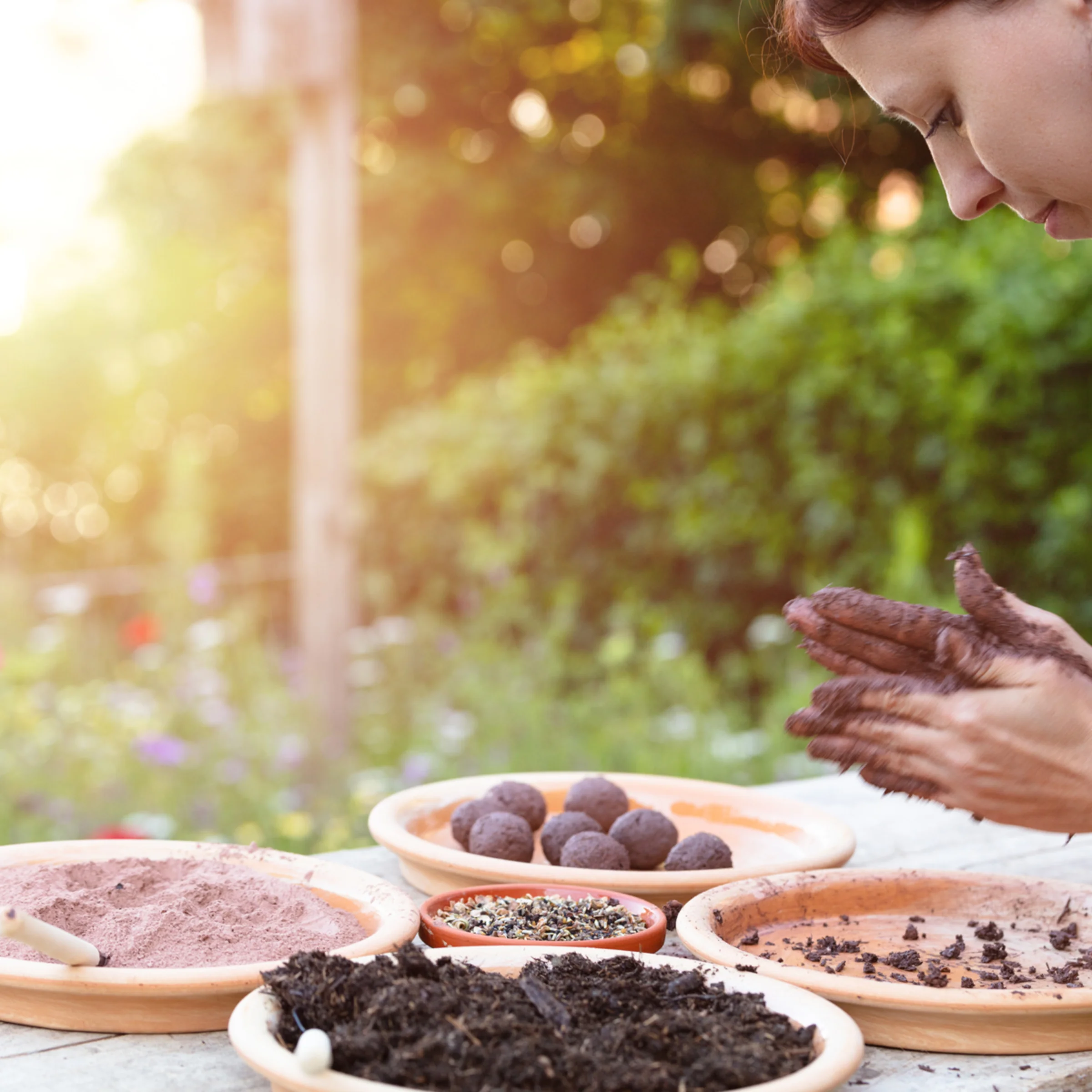 A woman crafting seed bombs from soil in a garden.