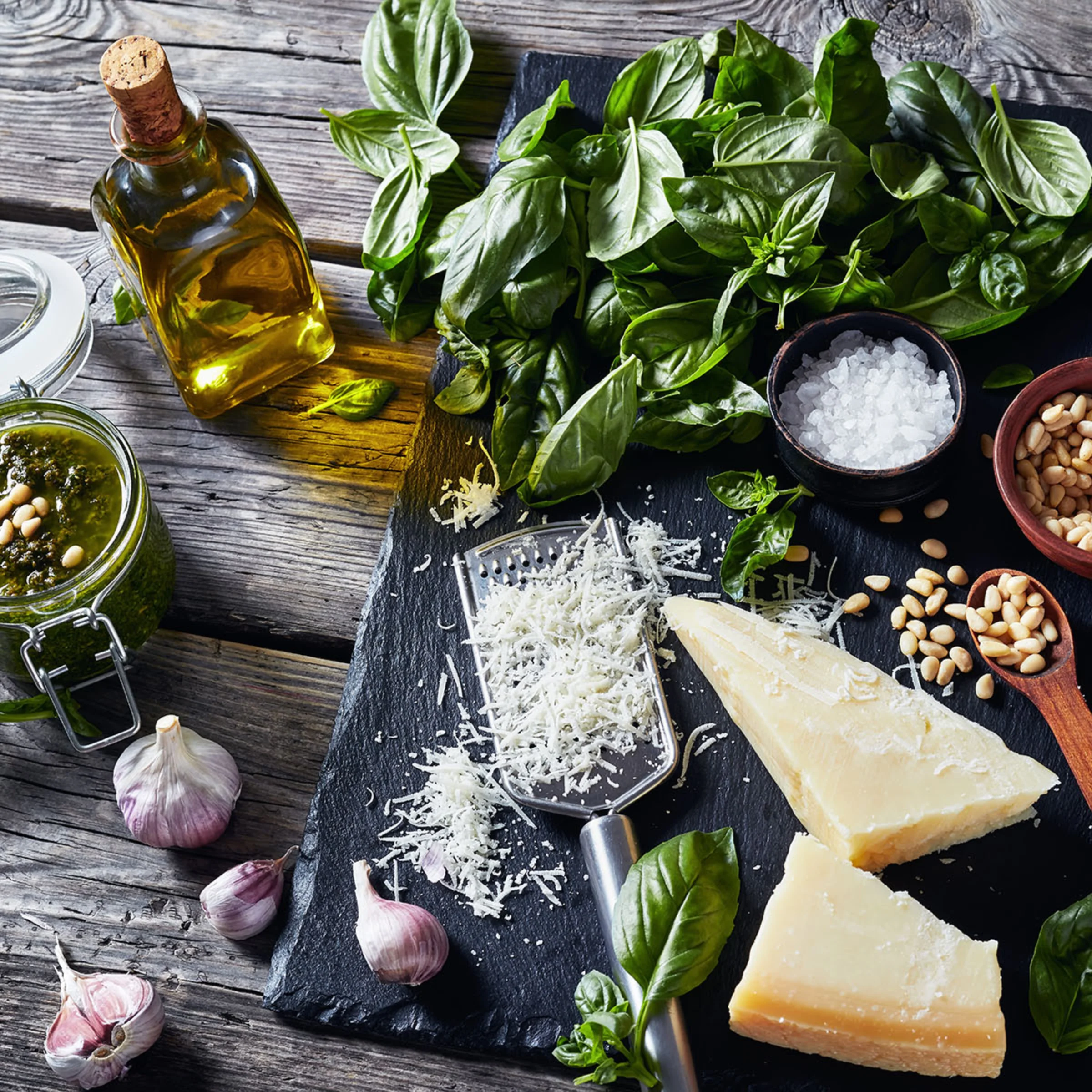 Ingredienti per pesto su un tavolo di legno: basilico, parmigiano e aglio.