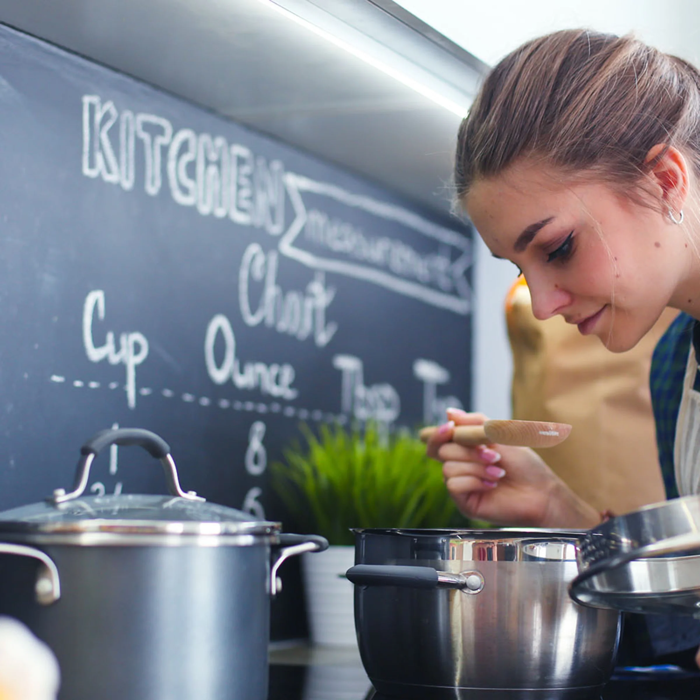 Una donna cucina in una cucina moderna con pentole e lavagna sullo sfondo, Nolte Kitchen.