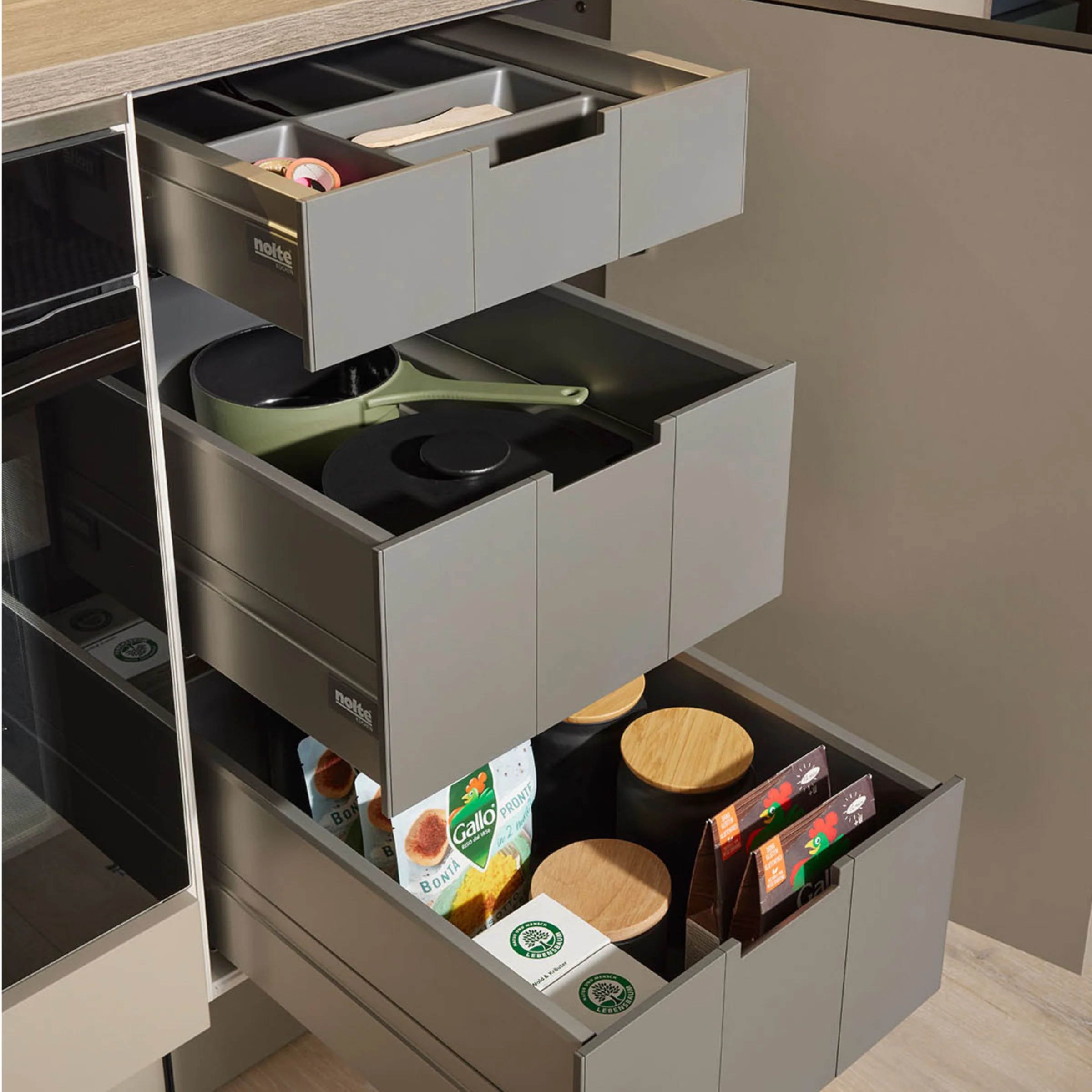 Armadi da cucina con cassetti aperti mostrano pentole e contenitori alimentari, design di Nolte Kitchen.