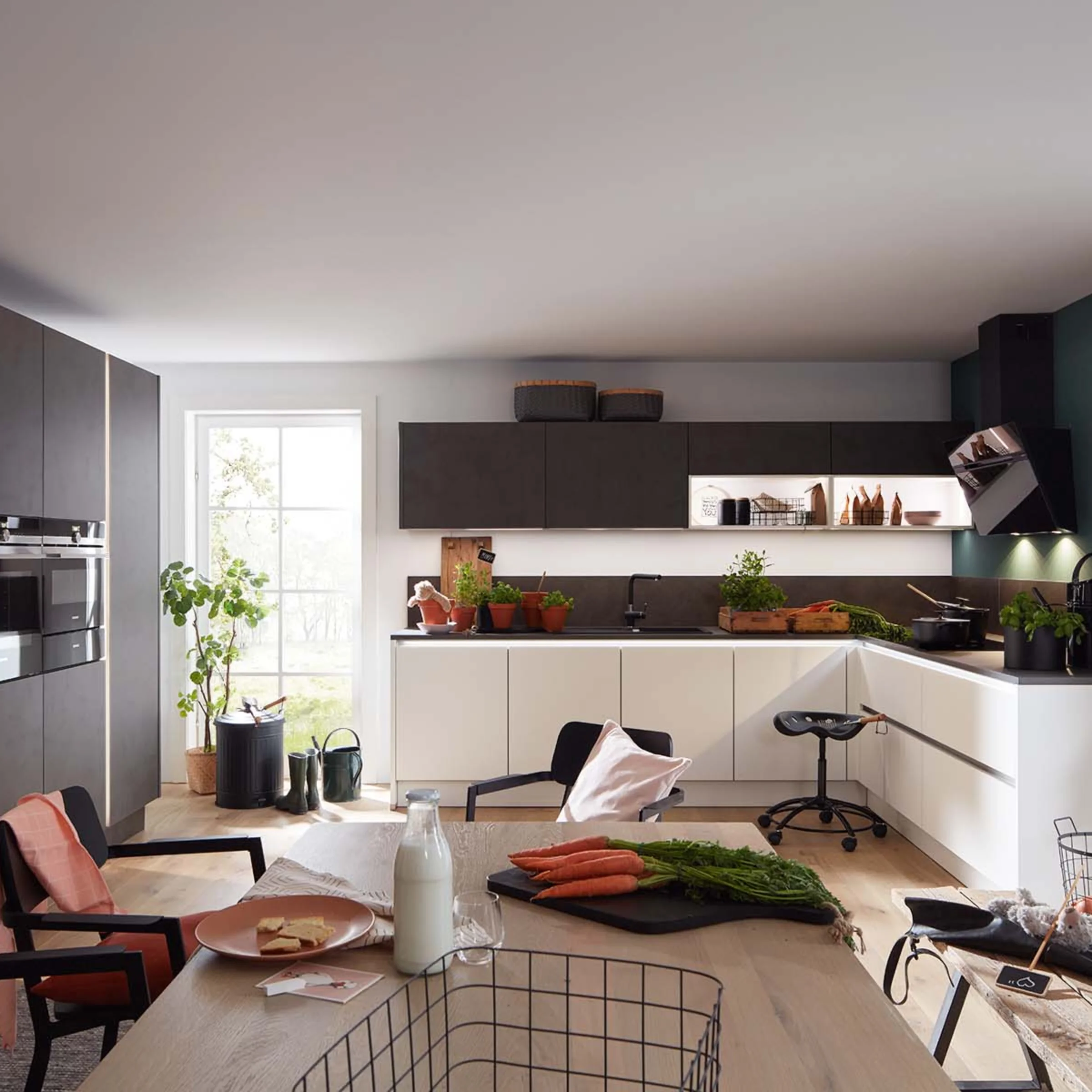 Cucina moderna con armadi bianchi e neri, piante e utensili sul piano di lavoro. Nolte Kitchen.