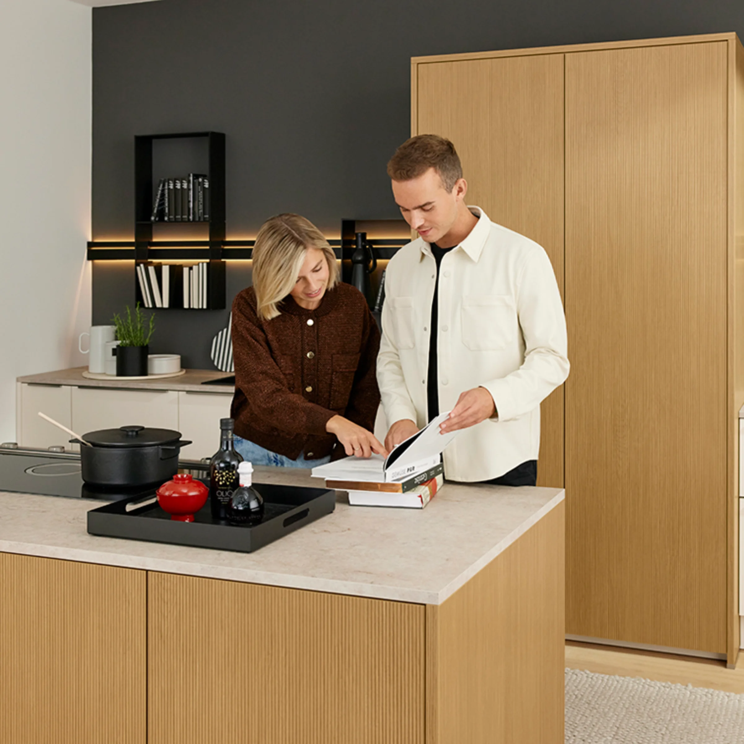 Una coppia guarda un libro di cucina in una cucina moderna con dettagli in legno, Nolte Kitchen.