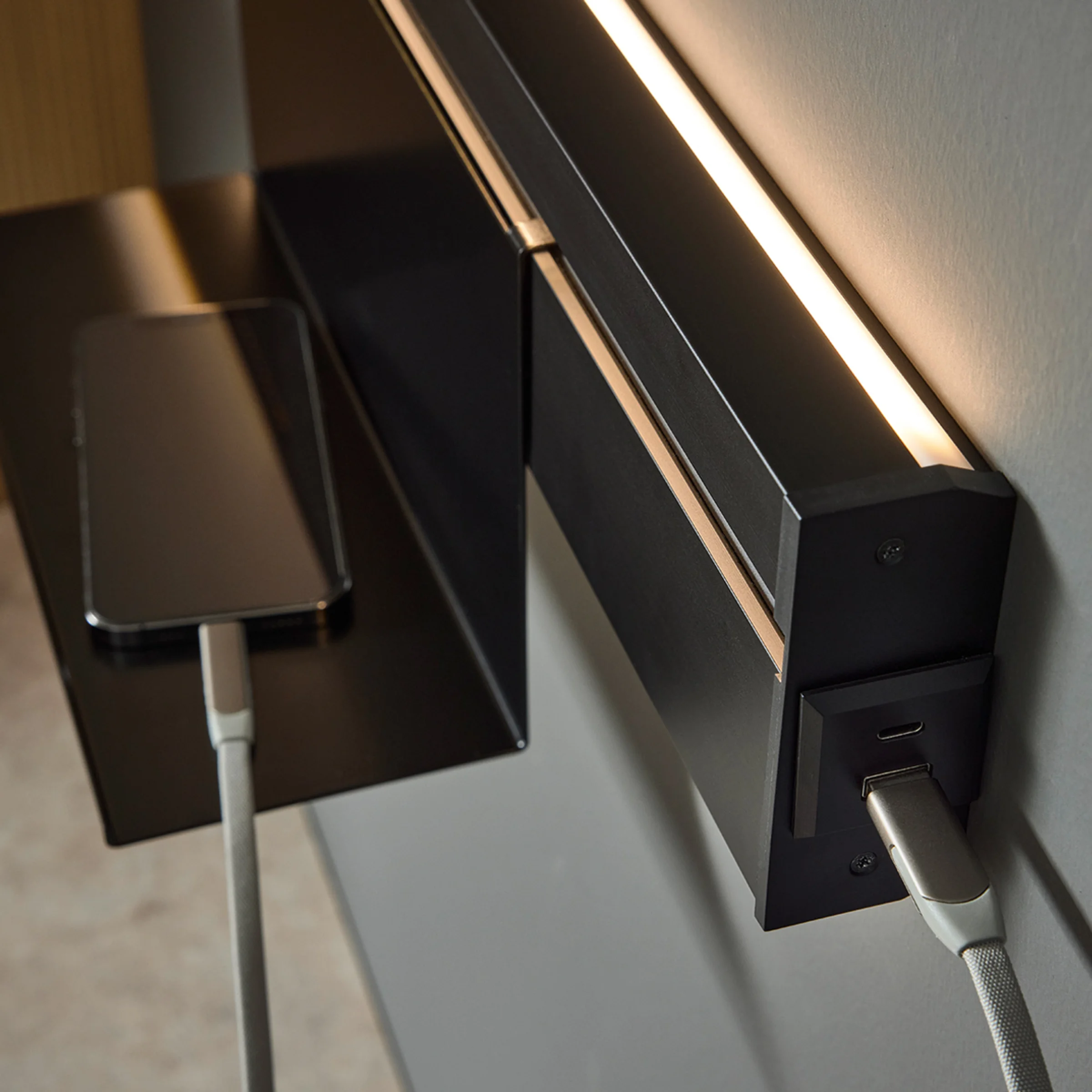 Uno smartphone si carica su uno scaffale con illuminazione integrata; design moderno di Nolte Living.