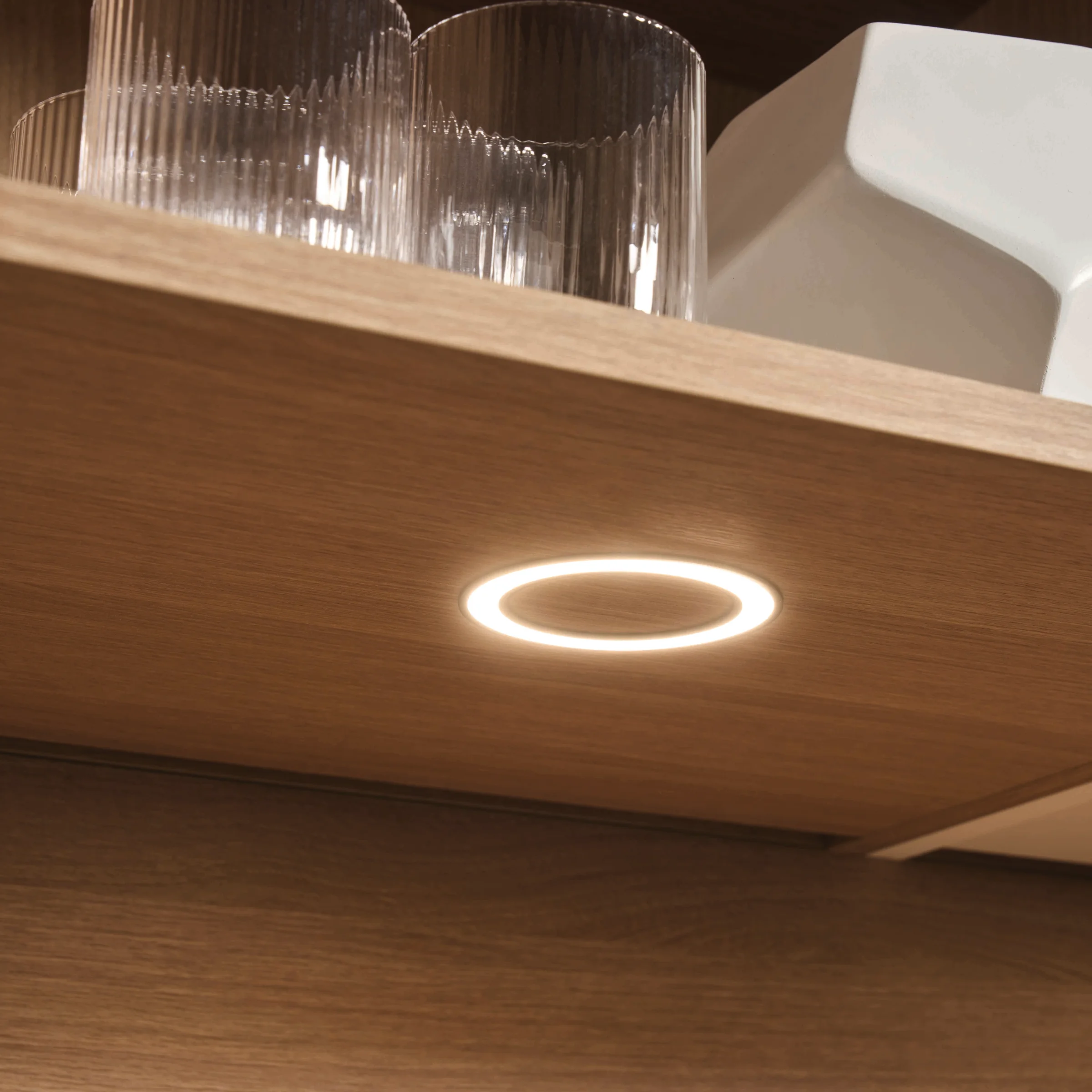 Un placard de cuisine en bois éclairé avec des verres et un bol blanc. Express Küchen.
