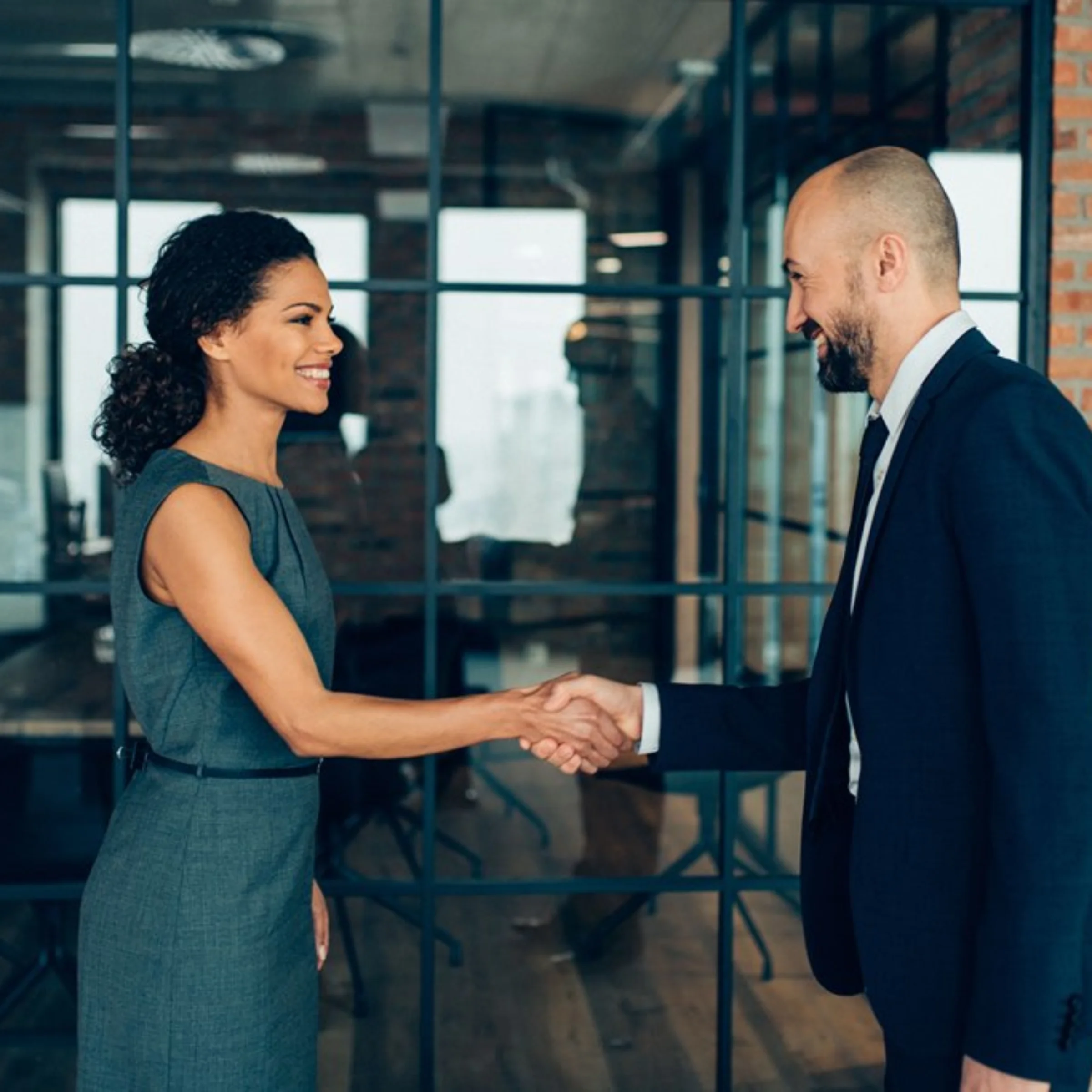Due persone in abiti da lavoro si stringono la mano in un ufficio moderno.