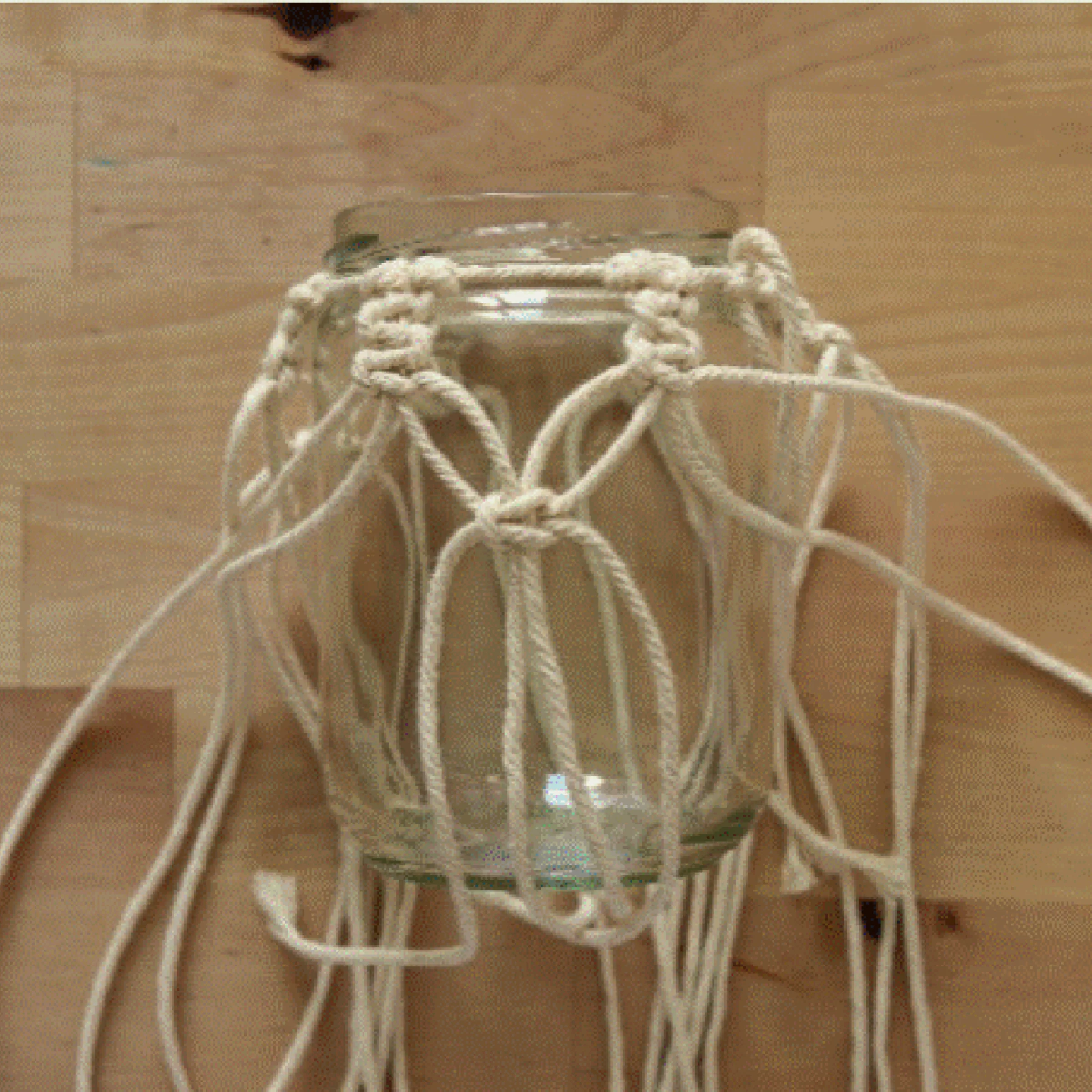 Vaso di vetro con supporto in macramè su un tavolo di legno.