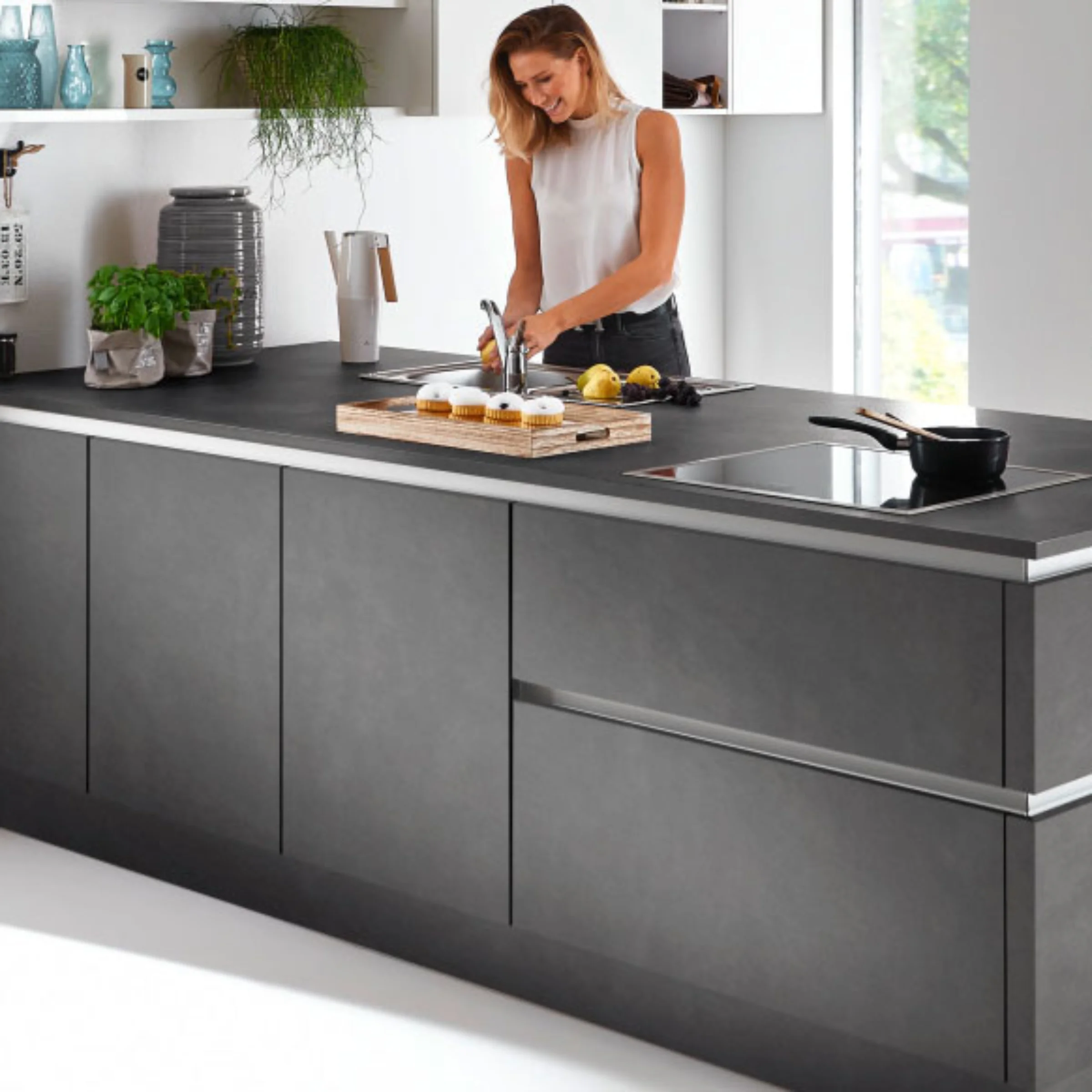 Una donna accanto a un'isola cucina moderna con superficie grigia. Nolte Kitchen.