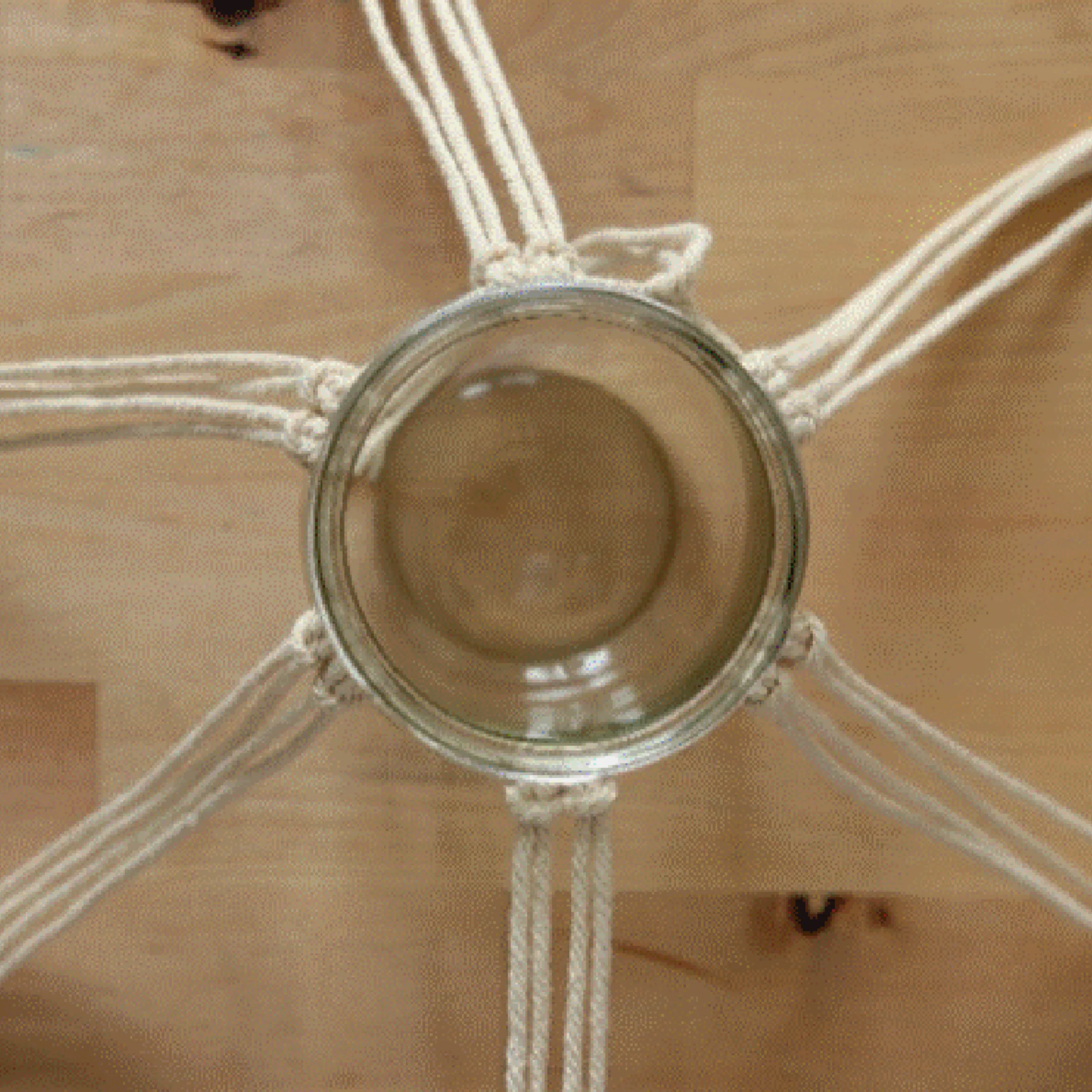 Ein Glas hängt in Makramee-Schnüren, die auf einem Holztisch liegen.