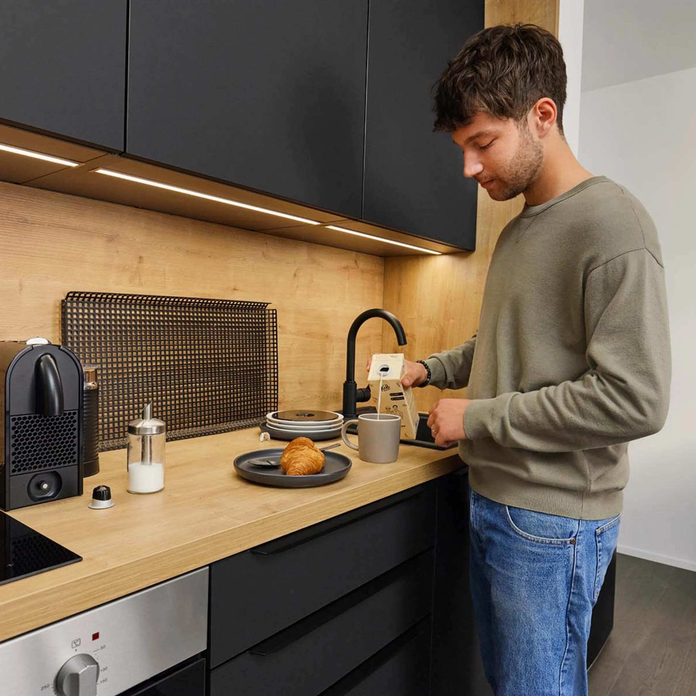 Un uomo prepara il caffè in una cucina moderna con accenti in legno e nero. Nolte Kitchen.
