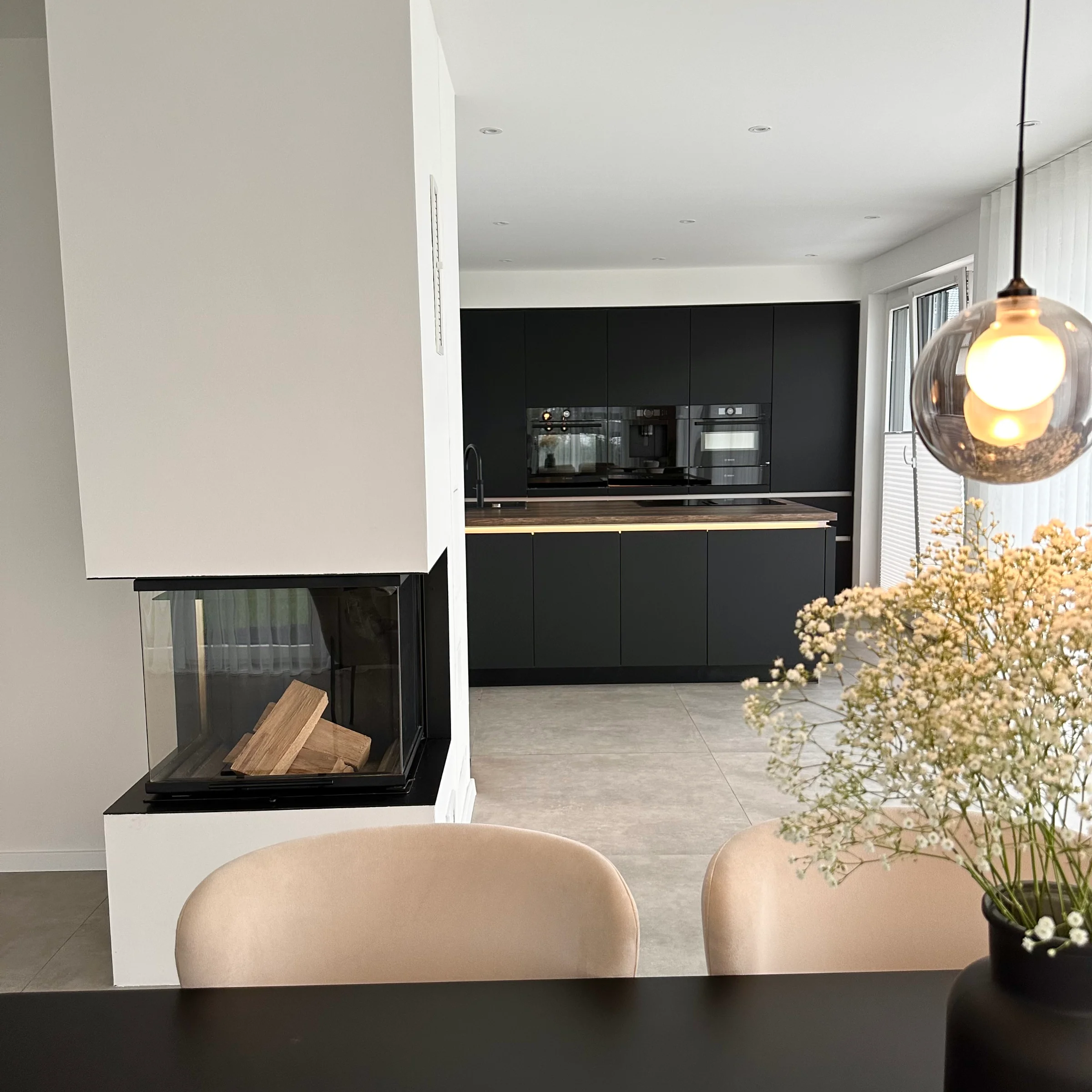 Cucina moderna con arredi neri e camino, in primo piano un tavolo da pranzo. Nolte Kitchen.