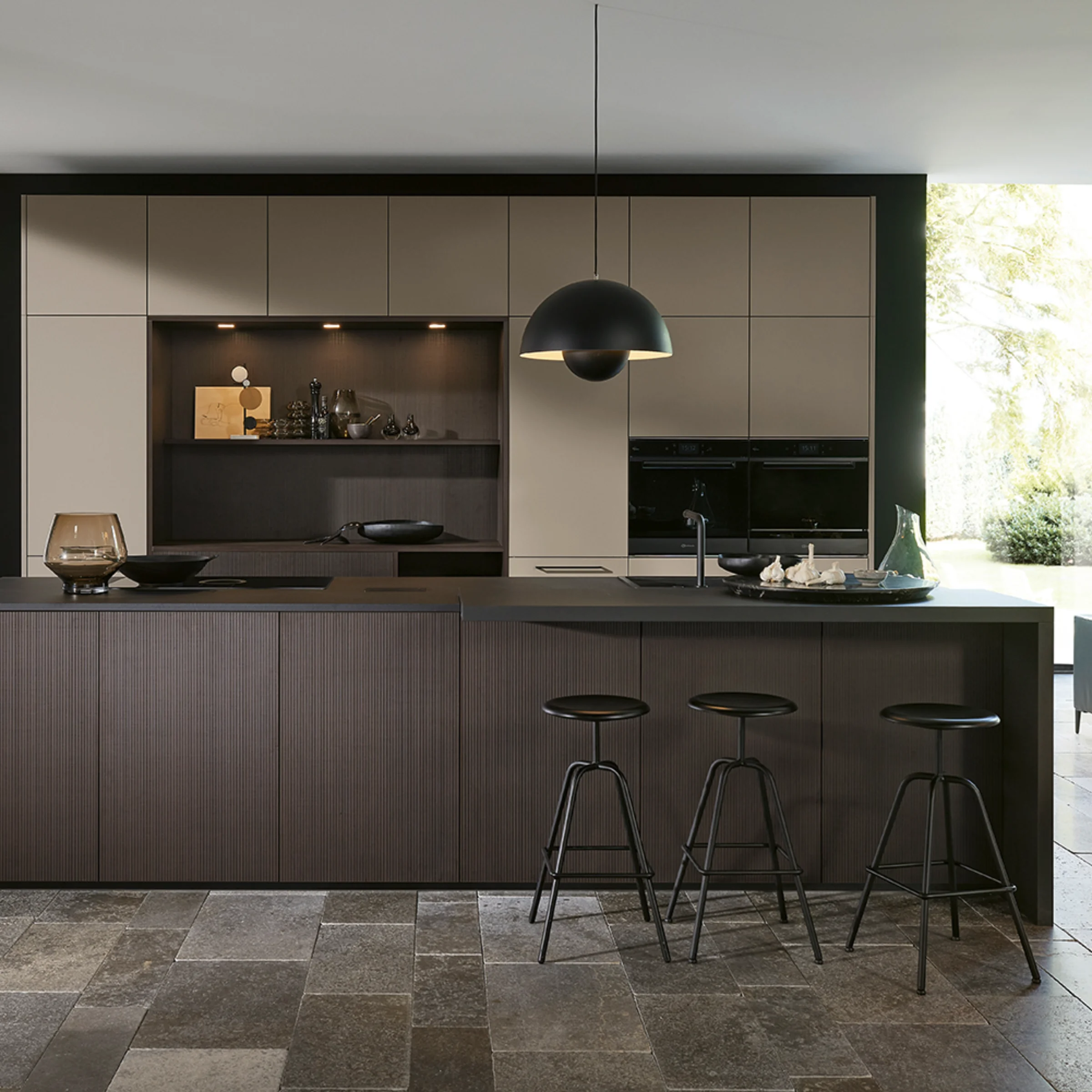Cucina moderna con isola scura e sgabelli in spazio aperto, circondata da grandi finestre. Nolte Kitchen.