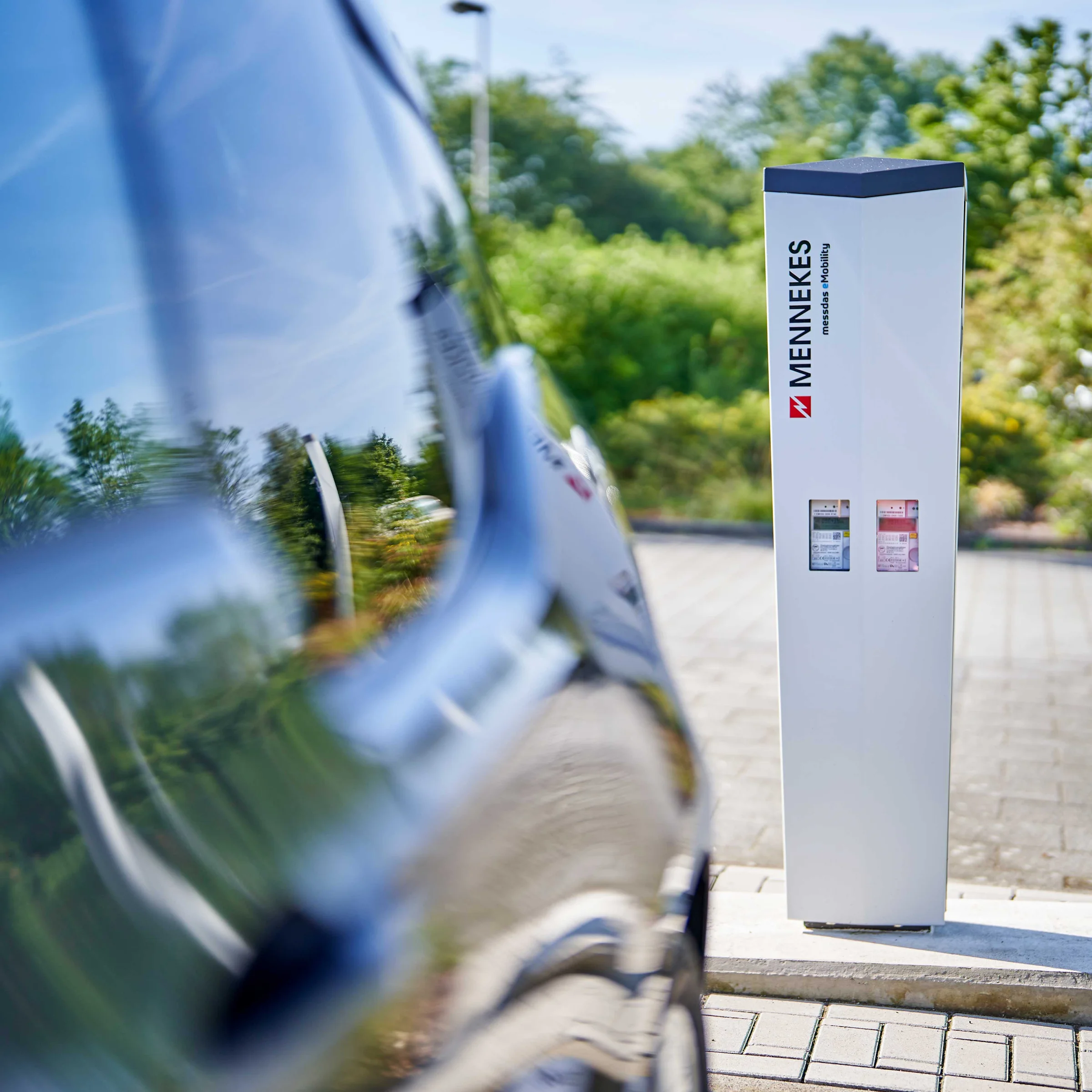 Auto elettrica in carica all'aperto, circondata da alberi. Nolte Kitchen.