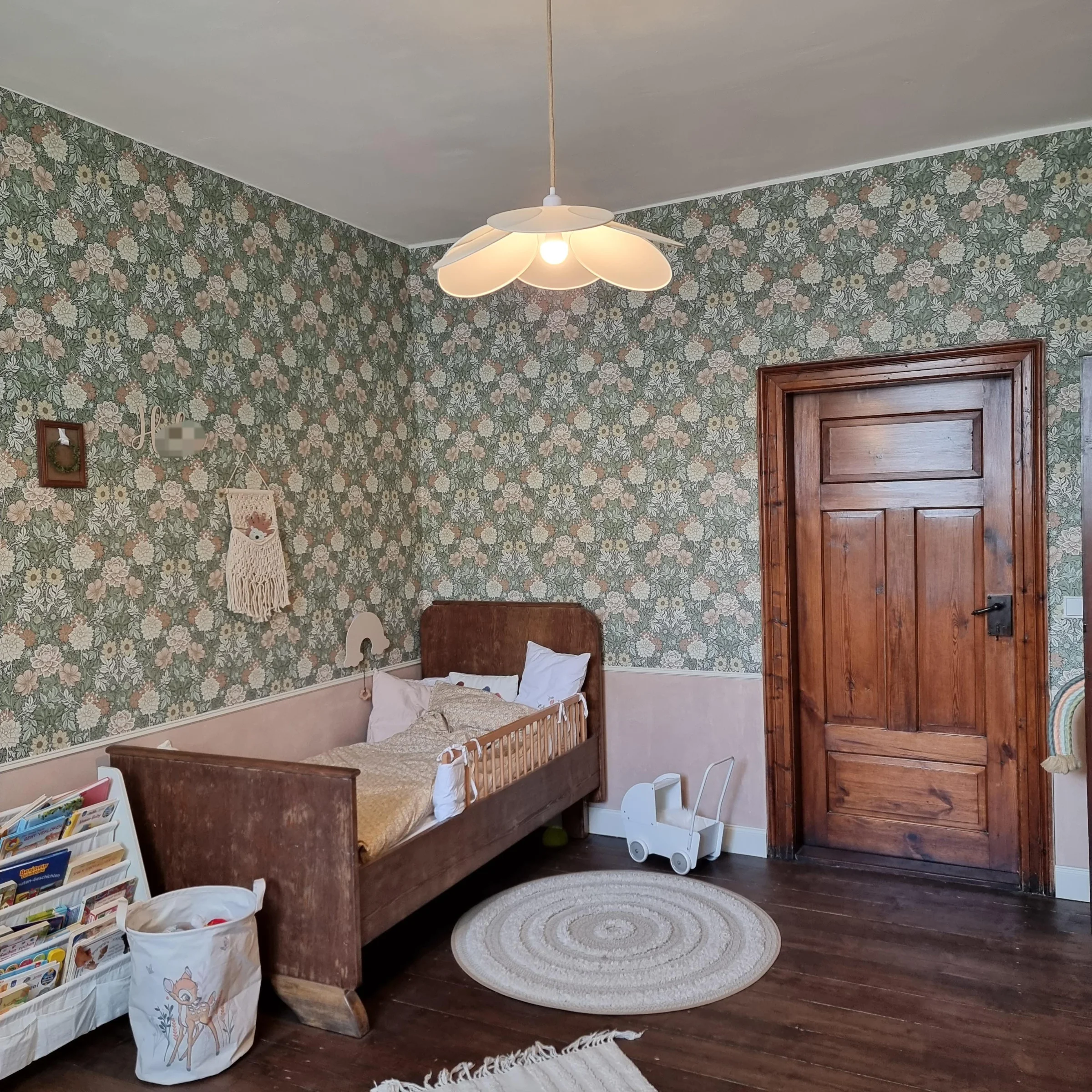Cameretta con letto in legno, carta da parati a fiori e tappeto rotondo su pavimento in legno.