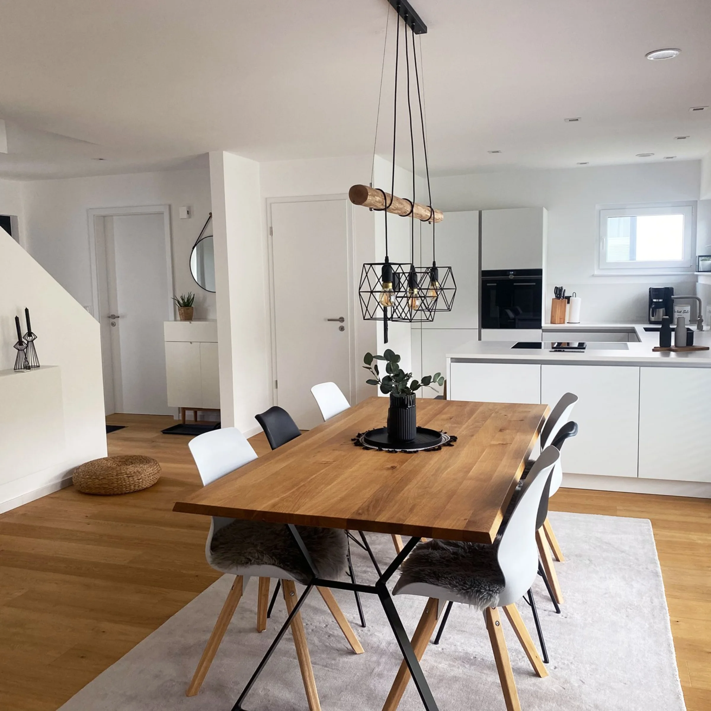 Sala da pranzo moderna con tavolo in legno e sedie bianche accanto a una cucina aperta di Nolte Kitchen.