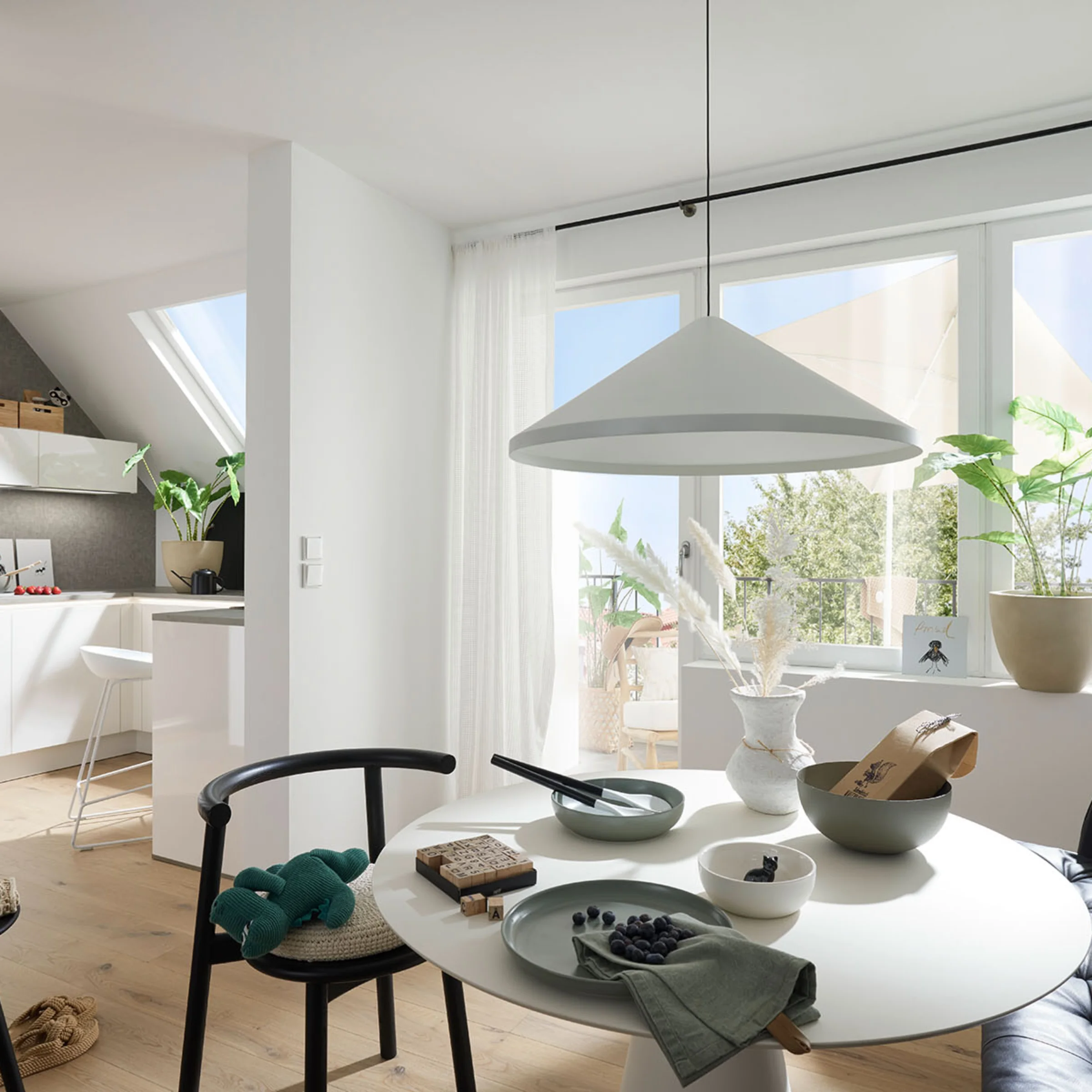 Un luminoso soggiorno con tavolo da pranzo e angolo cottura, circondato da piante, presenta Nolte Living.