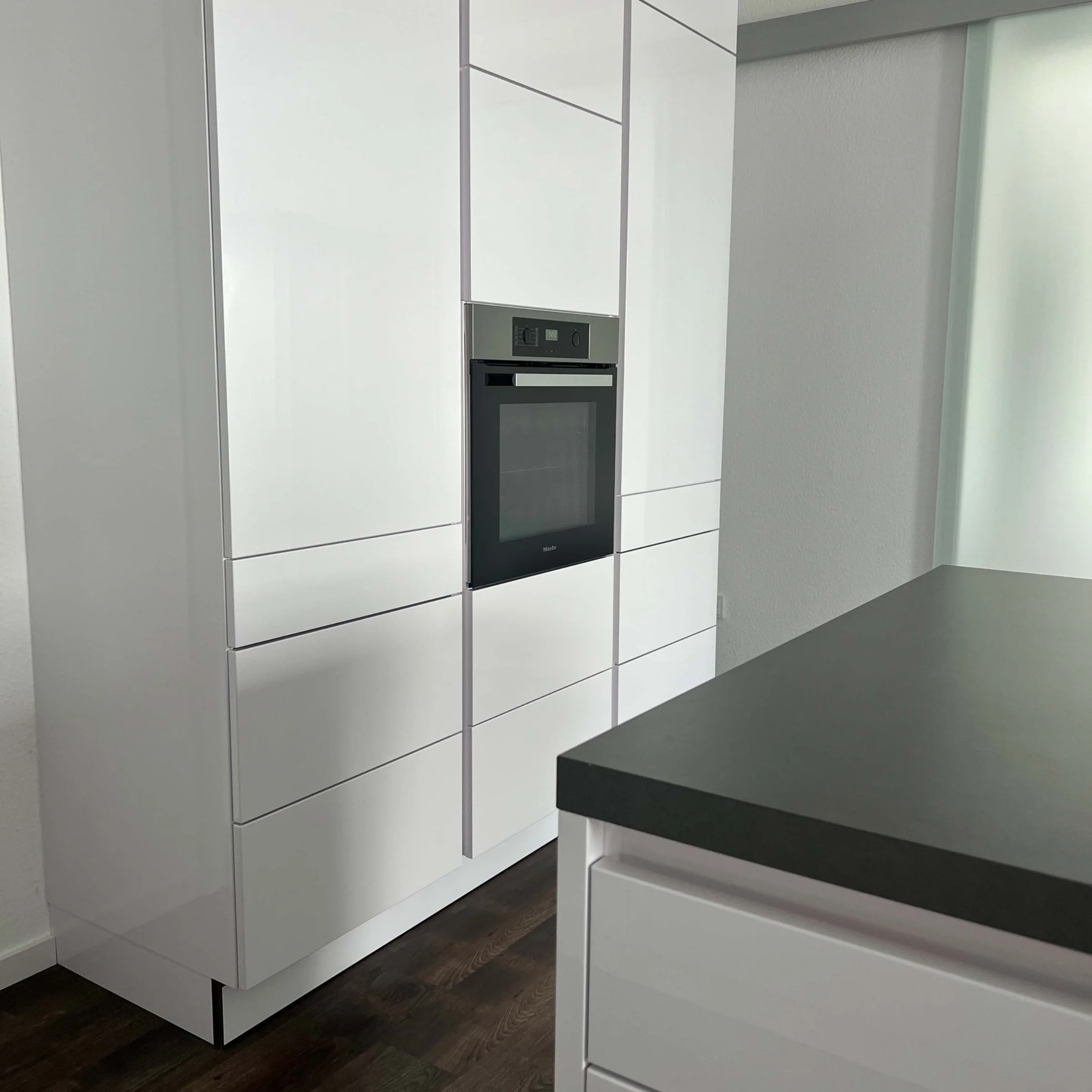 Cucina moderna bianca con forno integrato e pavimento in legno scuro, progettata da Nolte Kitchen.