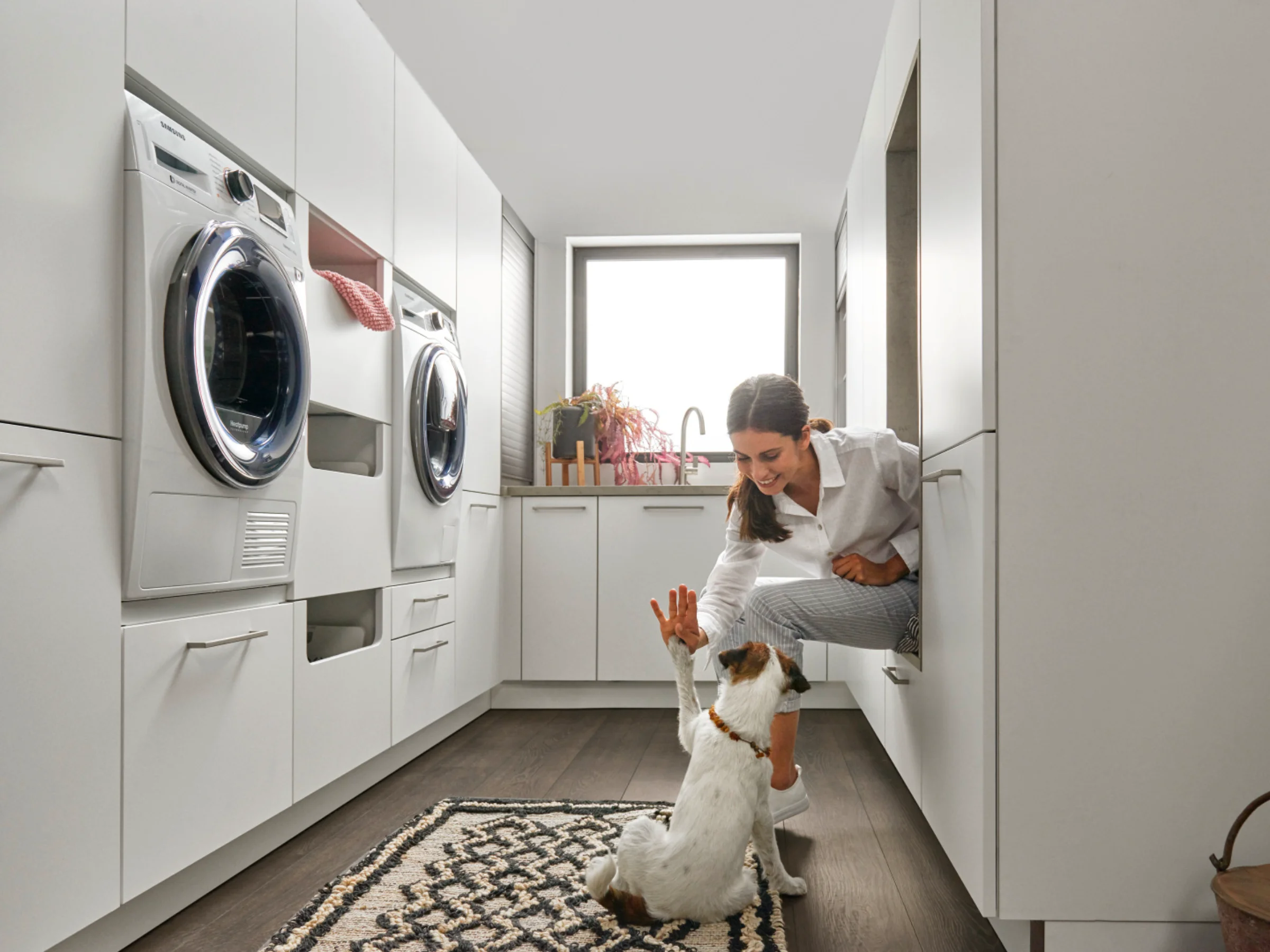 Una donna gioca con un cane in una moderna lavanderia di Nolte Utility Rooms.