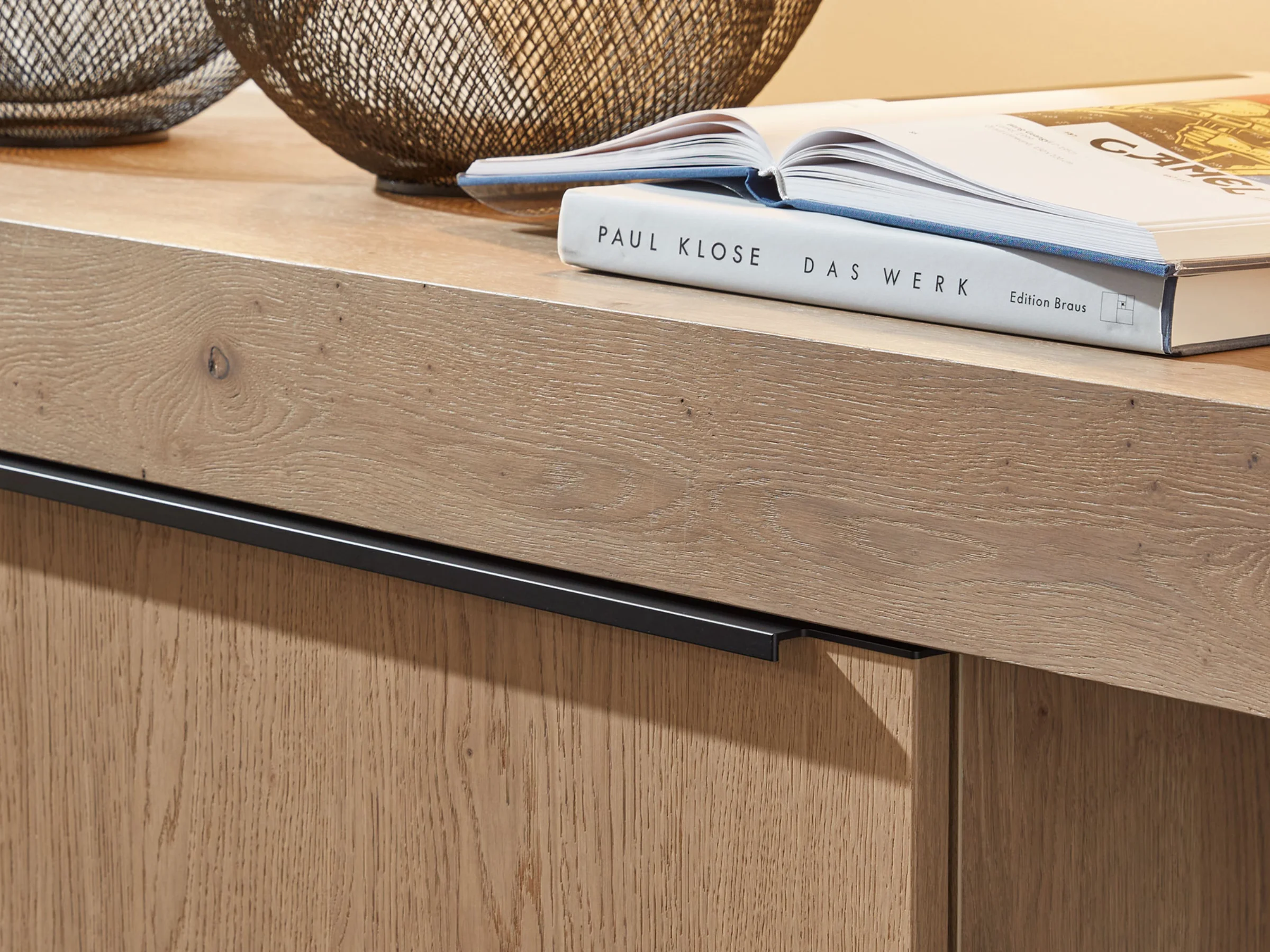 Armadio in legno con libri e cestini in filo sopra, parte della serie Nolte Living.