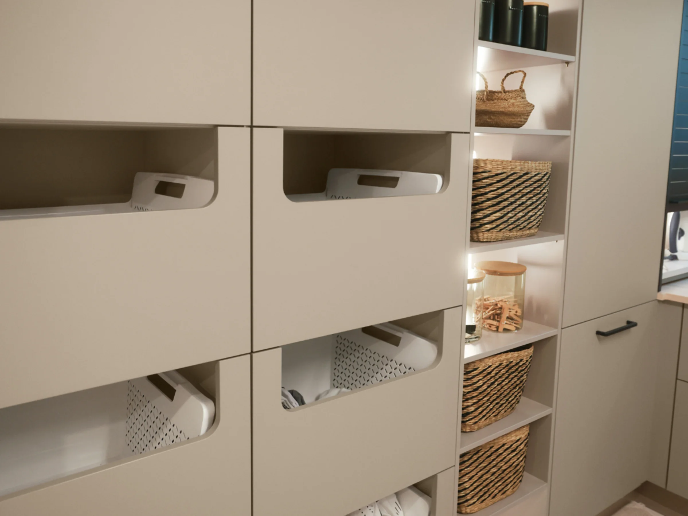 Una lavanderia con armadi beige e cesti, presentata da Nolte Utility Rooms.