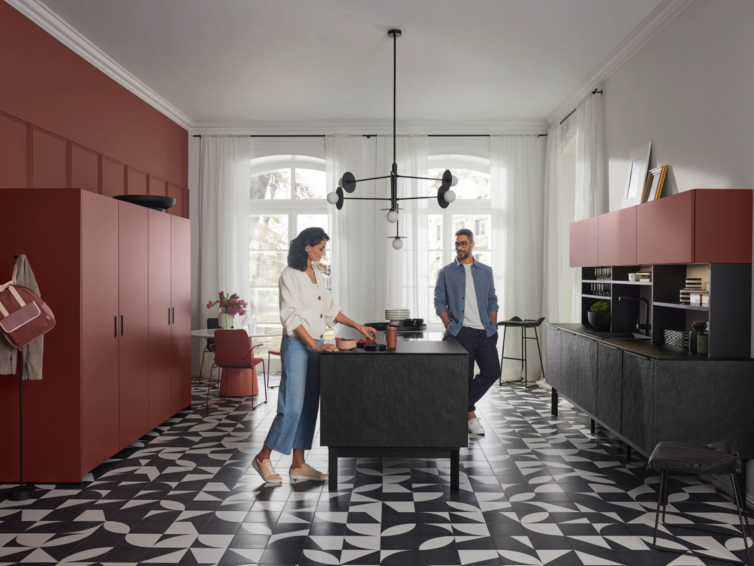 Cucina moderna Nolte con due persone, pavimento geometrico e armadi rossi.