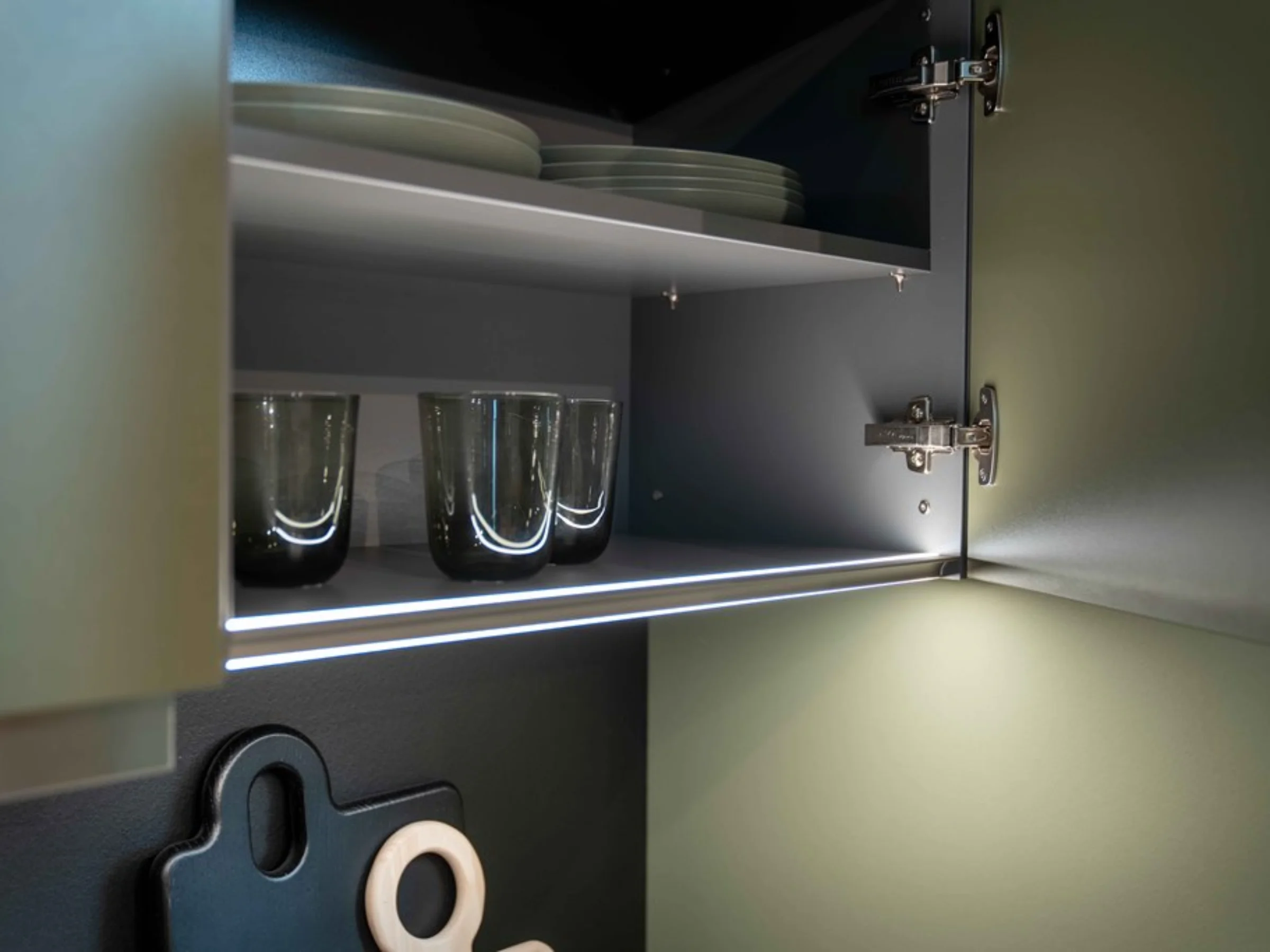 Un armadietto da cucina aperto con piatti e bicchieri, illuminato dall'interno. Nolte Kitchen.