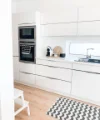 Cucina moderna e luminosa con armadi bianchi e tappeto, progettata con stile da Nolte Kitchen.