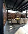Terrazza coperta con tavolo e quattro sedie in rattan, circondata da pareti a doghe di legno.
