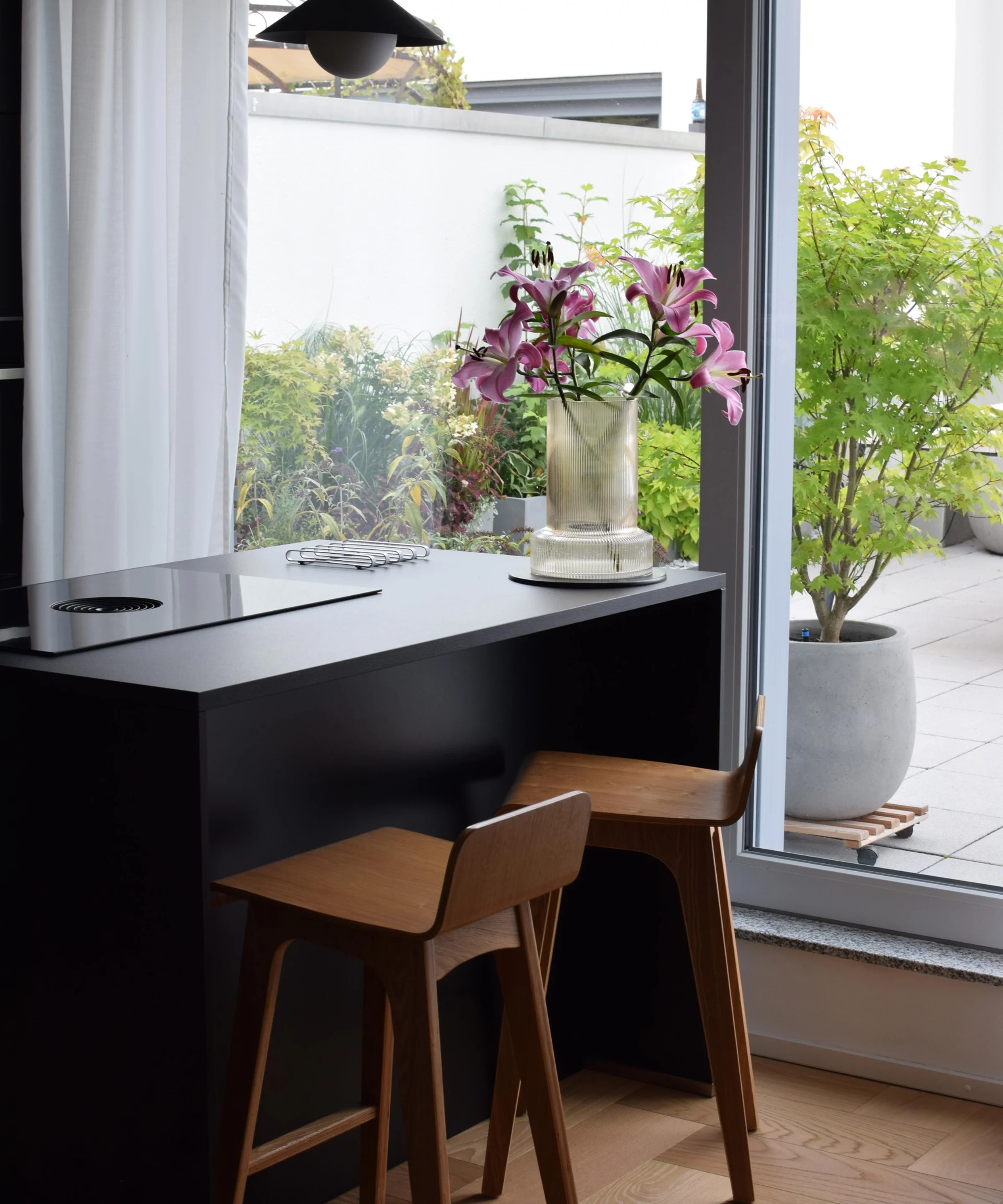 In una cucina moderna con grandi finestre, due sedie di legno sono davanti a un bancone nero. Nolte Kitchen.