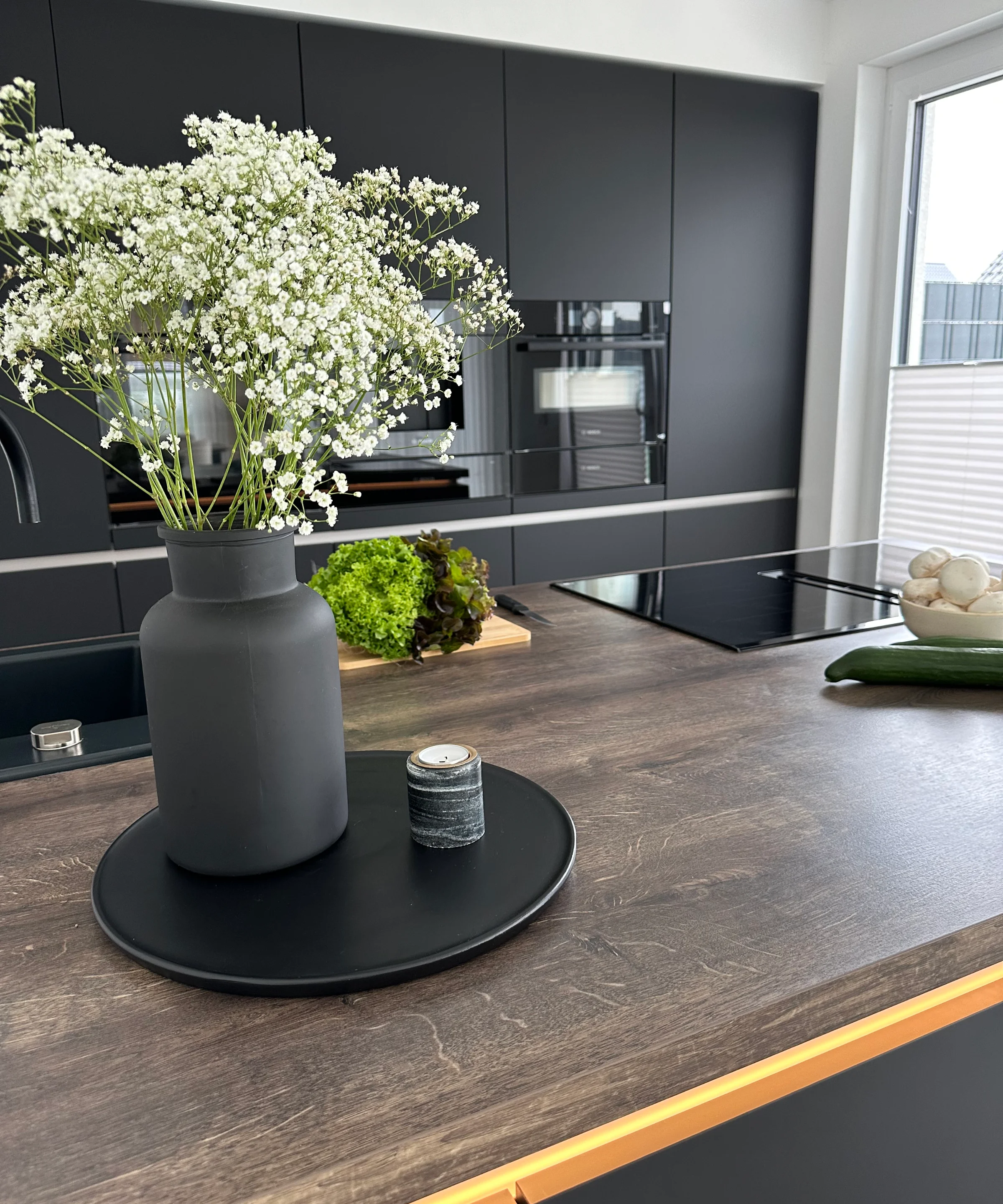 In una cucina moderna con armadi scuri, un vaso di fiori è sul piano di lavoro. Nolte Kitchen.