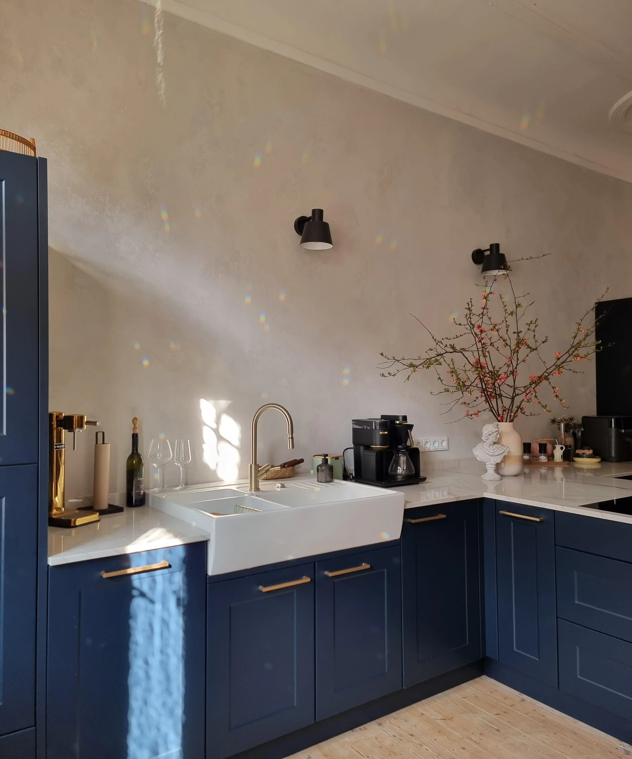 Cucina moderna con armadi blu e accenti dorati, illuminata dalla luce solare. Nolte Kitchen.