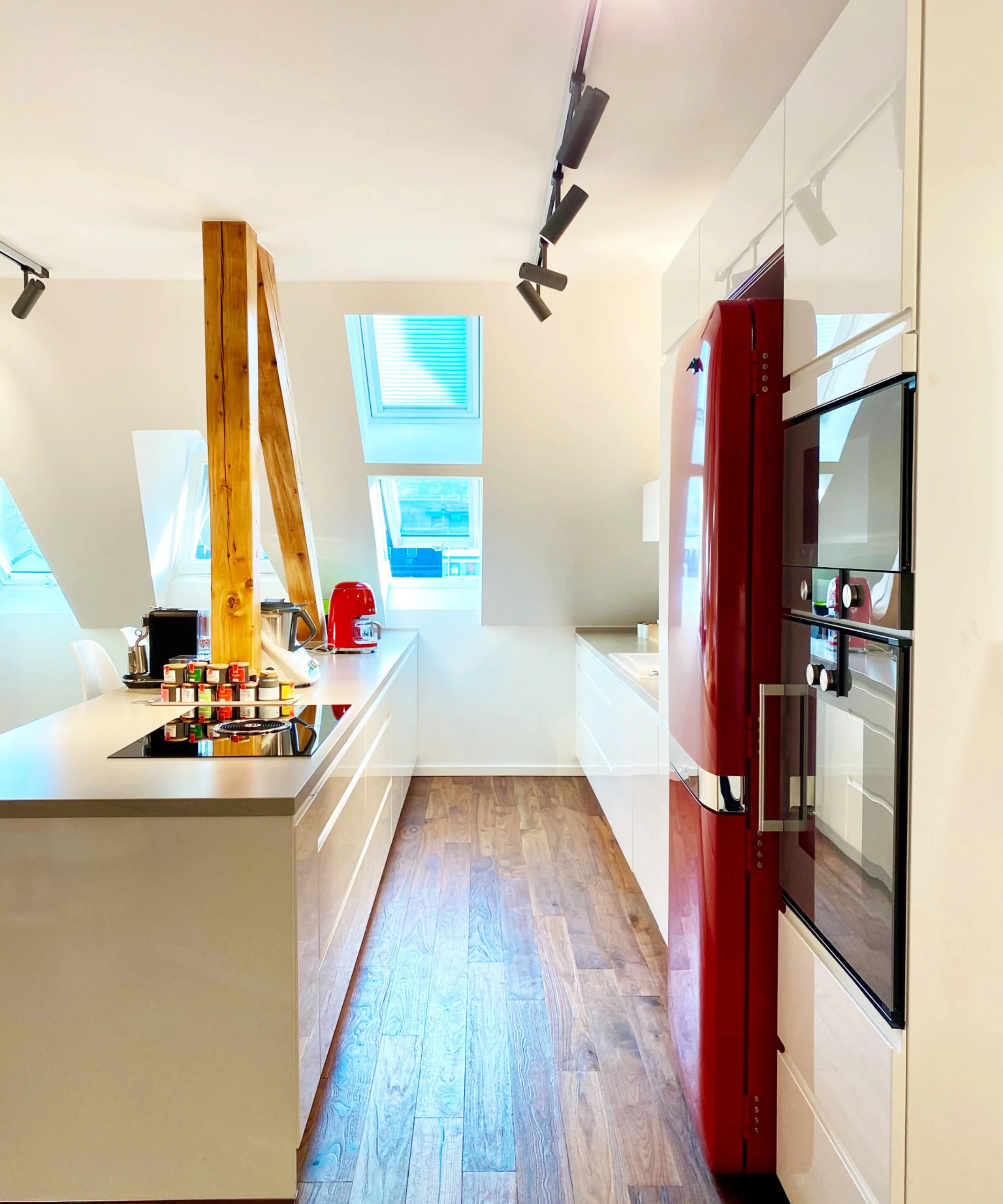 Cucina moderna con accenti rossi ed elementi in legno, illuminata da lucernari. Nolte Kitchen.