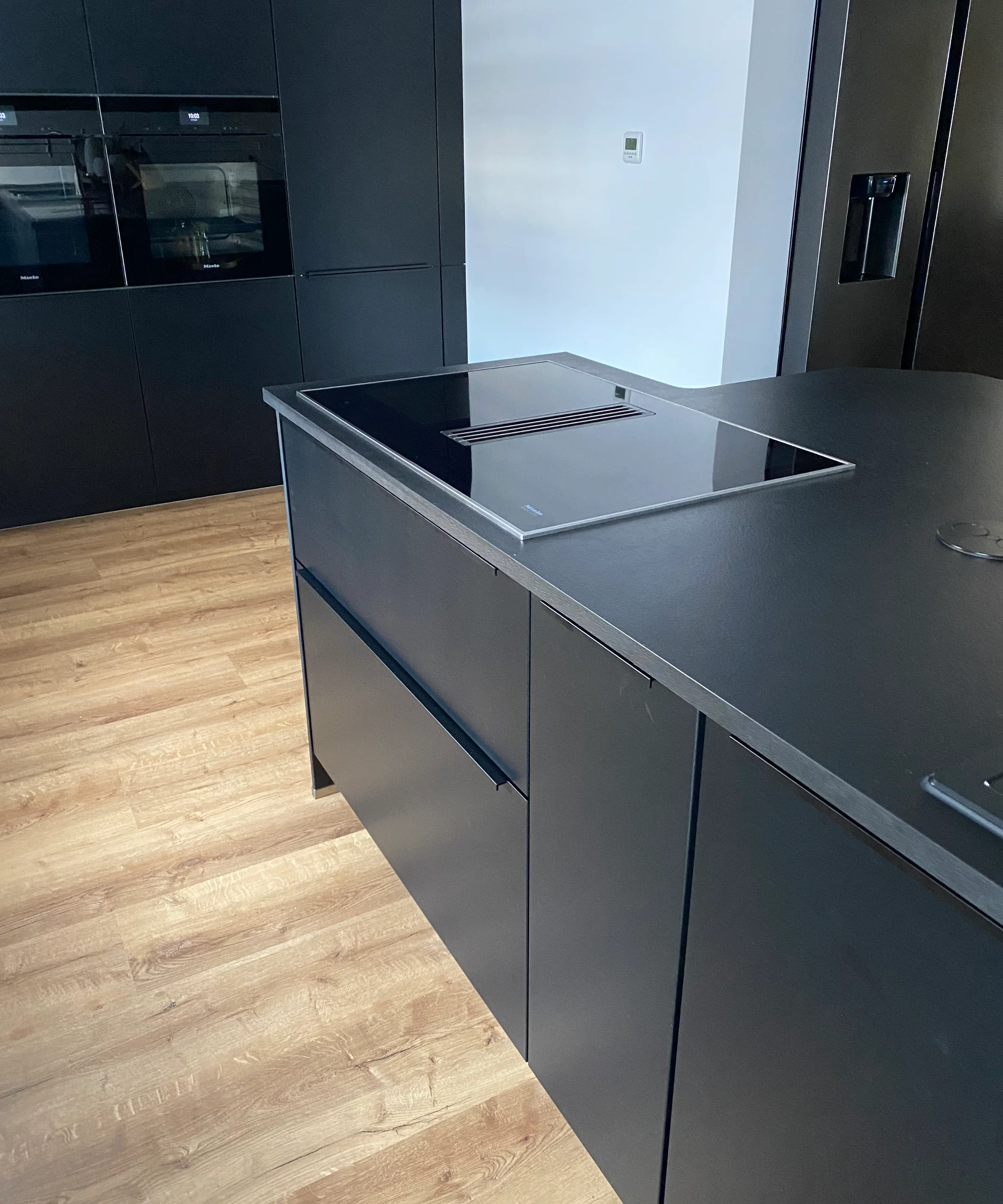 Cucina moderna con design nero e pavimento in legno, dotata di cucine Nolte.