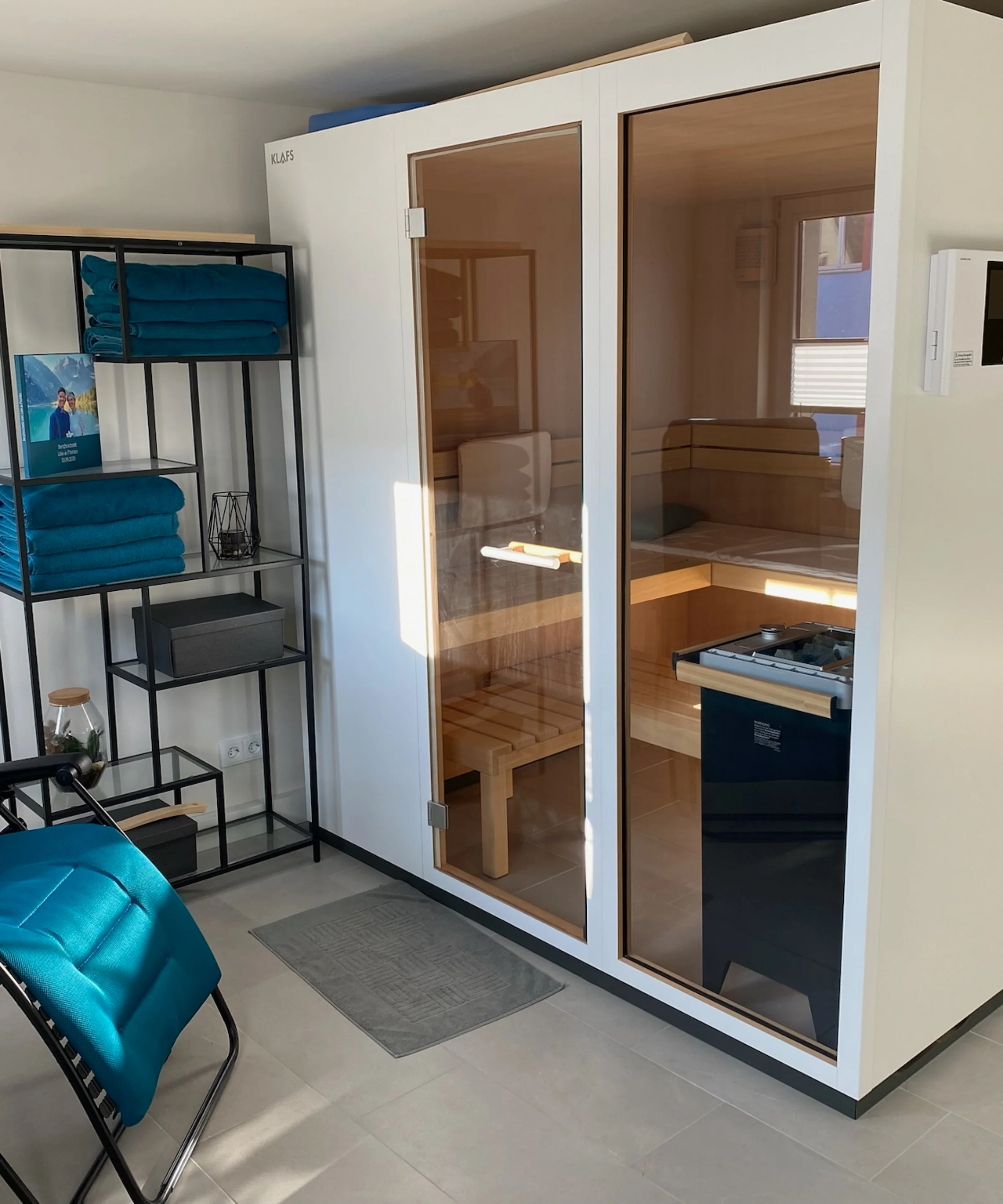 Sauna moderna con sedia a sdraio blu e scaffali, parte di Nolte SPA.
