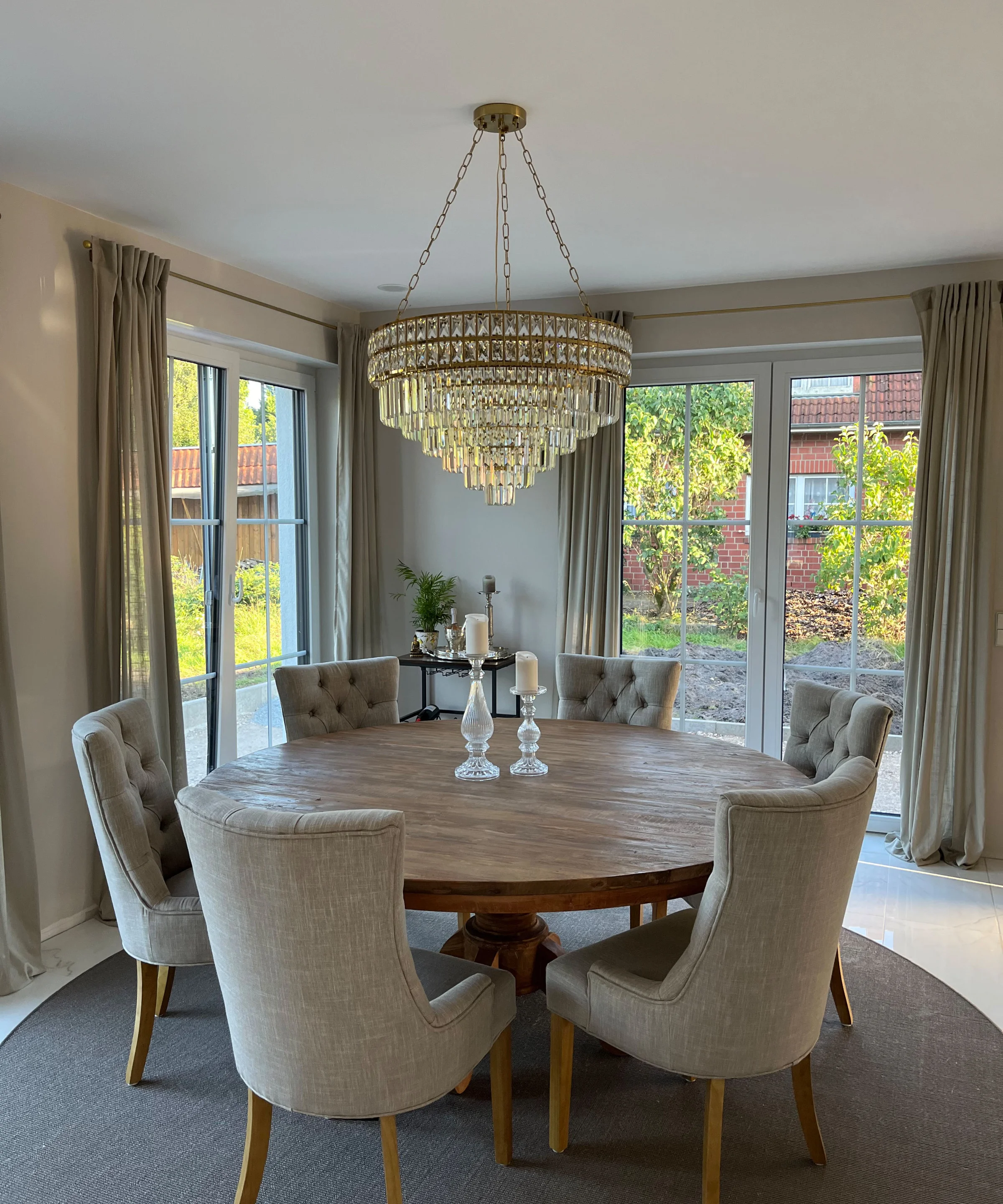Sala da pranzo elegante con tavolo rotondo in legno e sedie imbottite sotto un lampadario. Nolte Living.