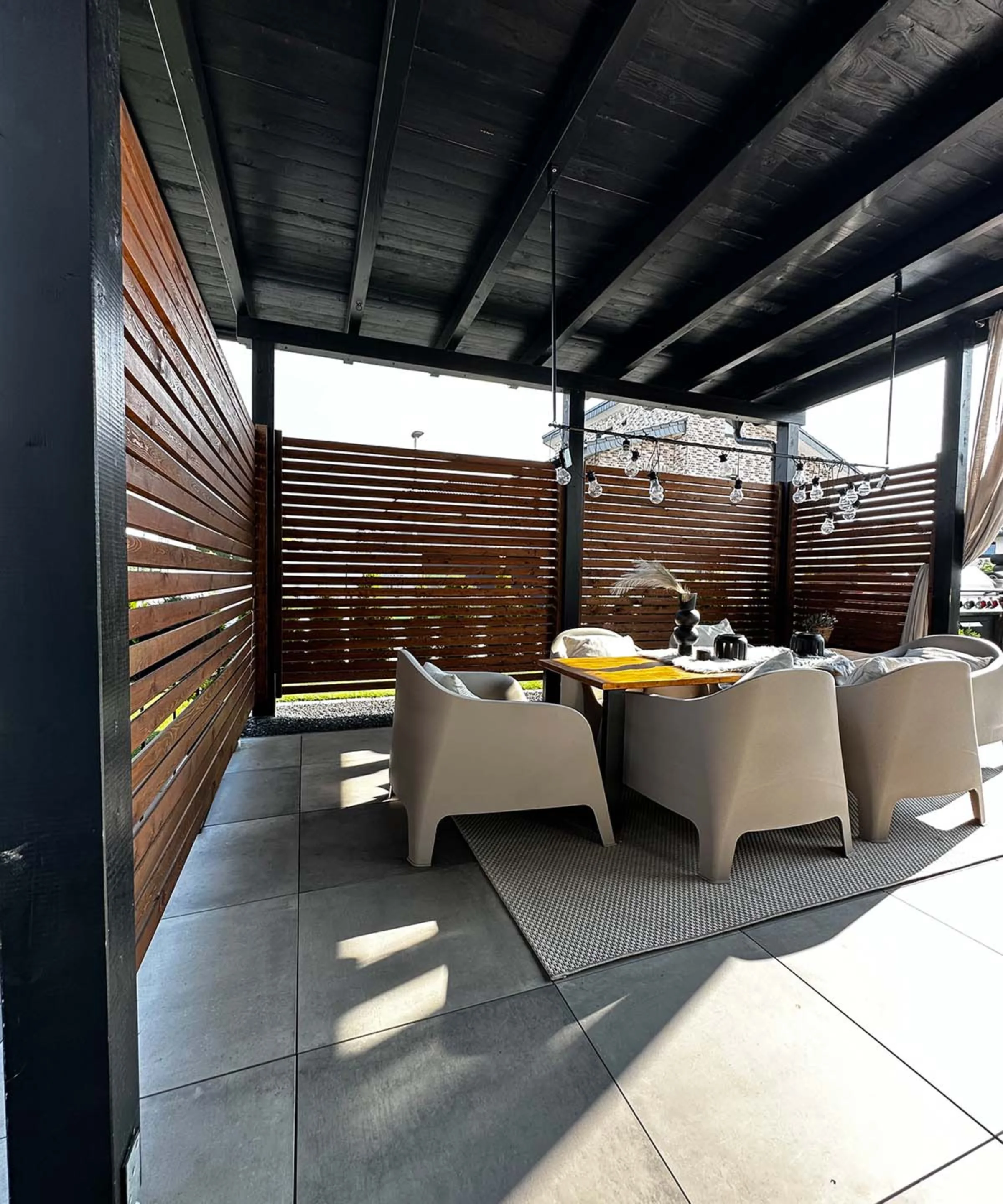 Terrazza coperta con tavolo e quattro sedie in rattan, circondata da pareti a doghe di legno.