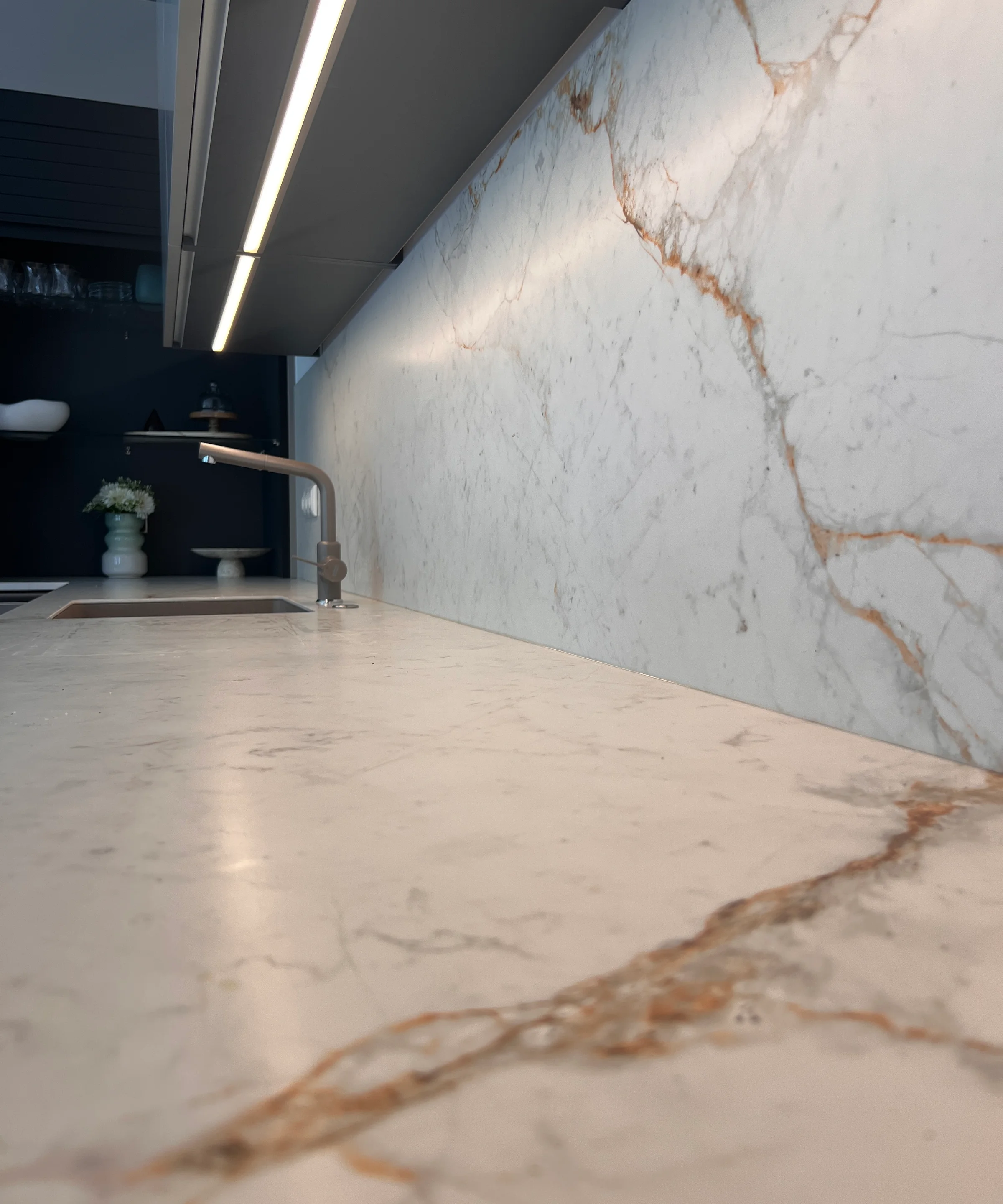 Cucina moderna con piano in marmo e lavello, illuminata da luce sottopensile. Nolte Kitchen.