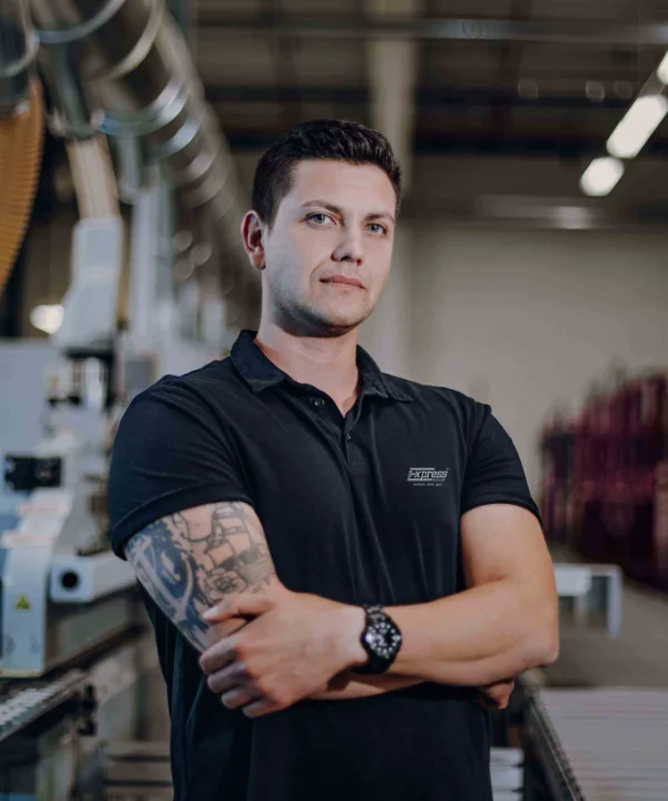 Eine Person steht in einer industriellen Umgebung mit Maschinen im Hintergrund.