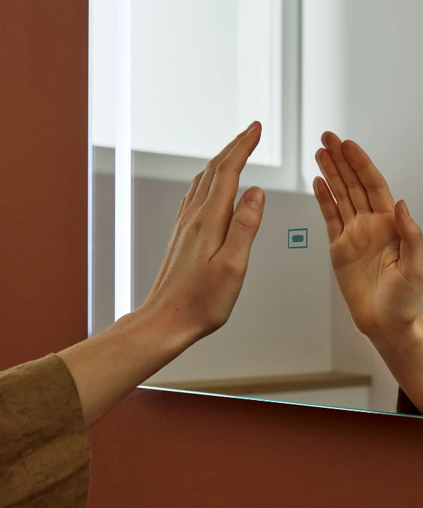 Una mano tocca uno specchio illuminato in un bagno moderno, Nolte SPA.