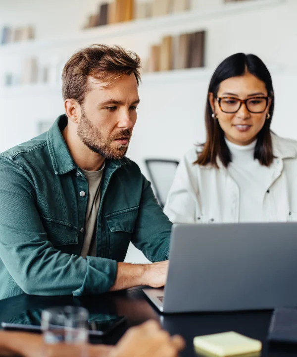 Tre persone sedute a un tavolo lavorano insieme su un laptop.